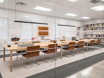 A series of brown leather and stainless steel chairs arranged at a large wooden table in a brightly lit reading room at the MillerKnoll archives