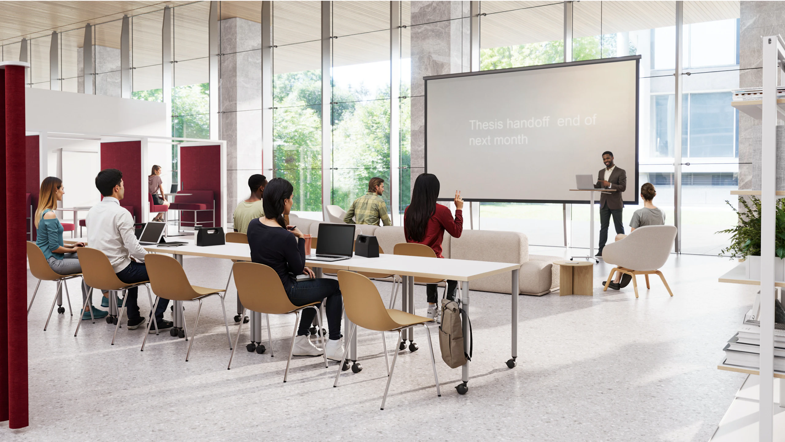 People seated in a modern classroom watching a presentation on a large screen. Some have laptops open on tables.