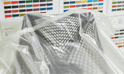 A black Sayl Chair by Herman Miller covered by a think plastic covering. A range of colorful fabric swatches are seen in the background.