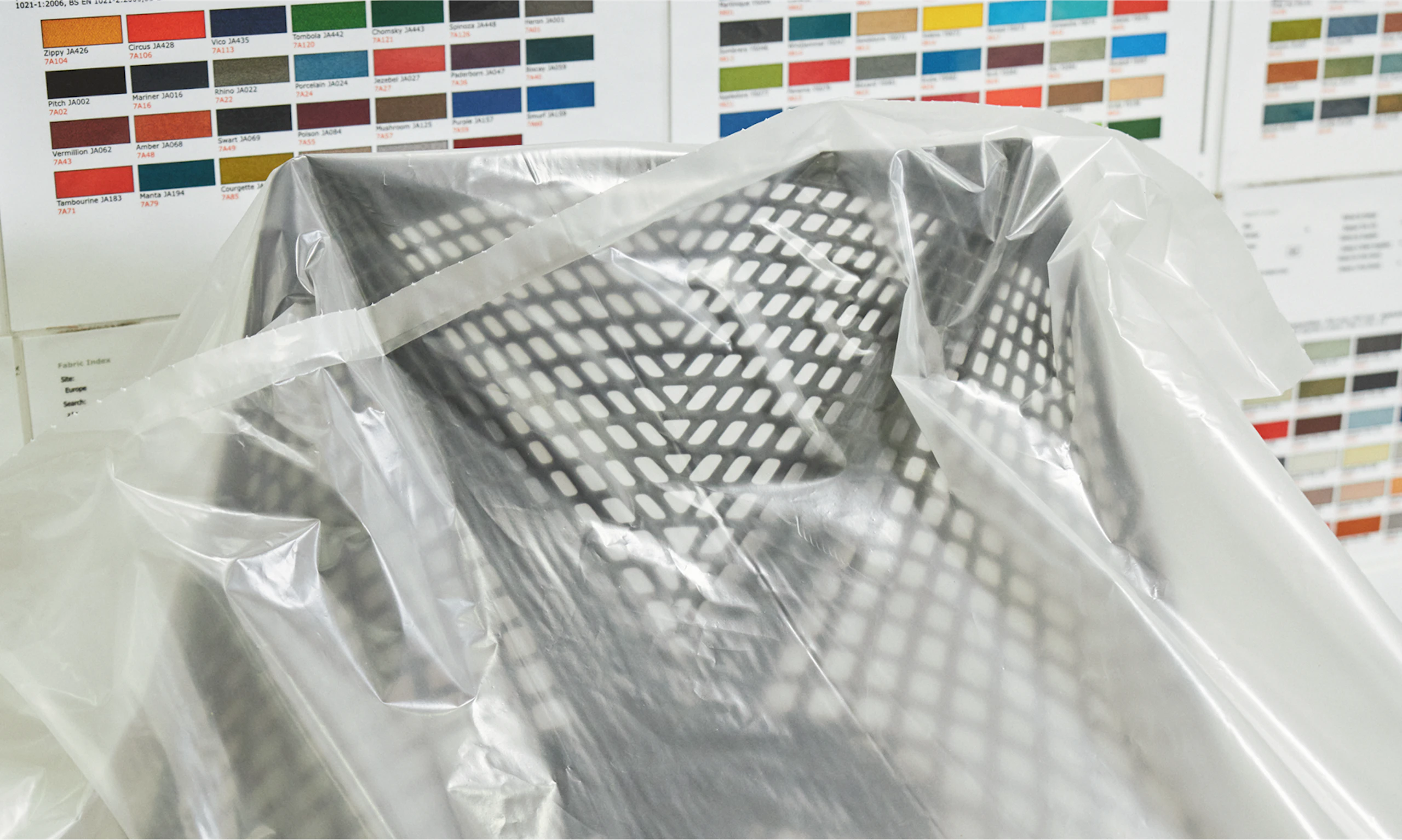A black Sayl Chair by Herman Miller covered by a think plastic covering. A range of colorful fabric swatches are seen in the background.