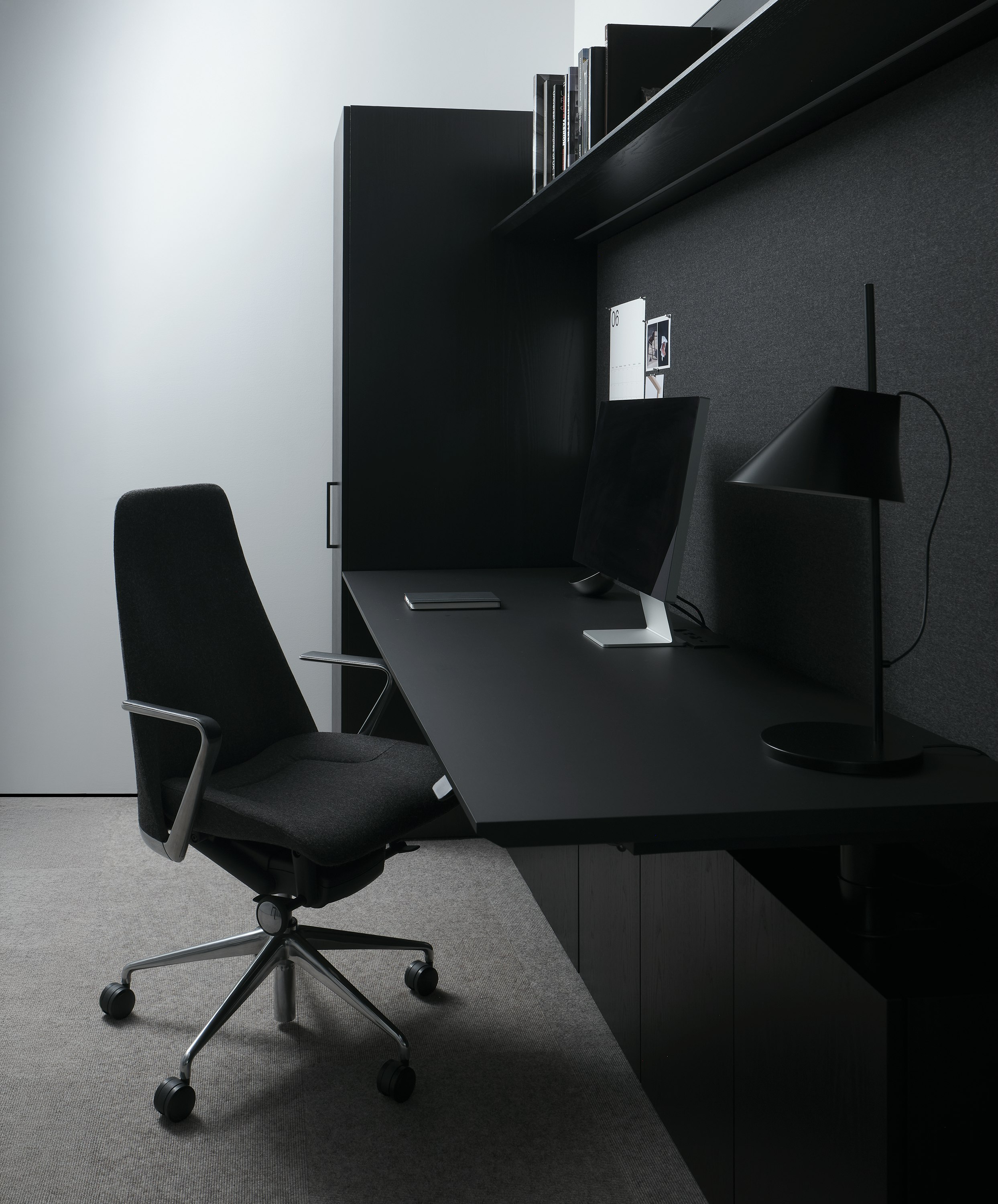 Geiger One Private Office in Ebonized Flat Cut Ash with a black soft-touch laminate height-adjustable work surface and Taper Chair, viewed from the side.