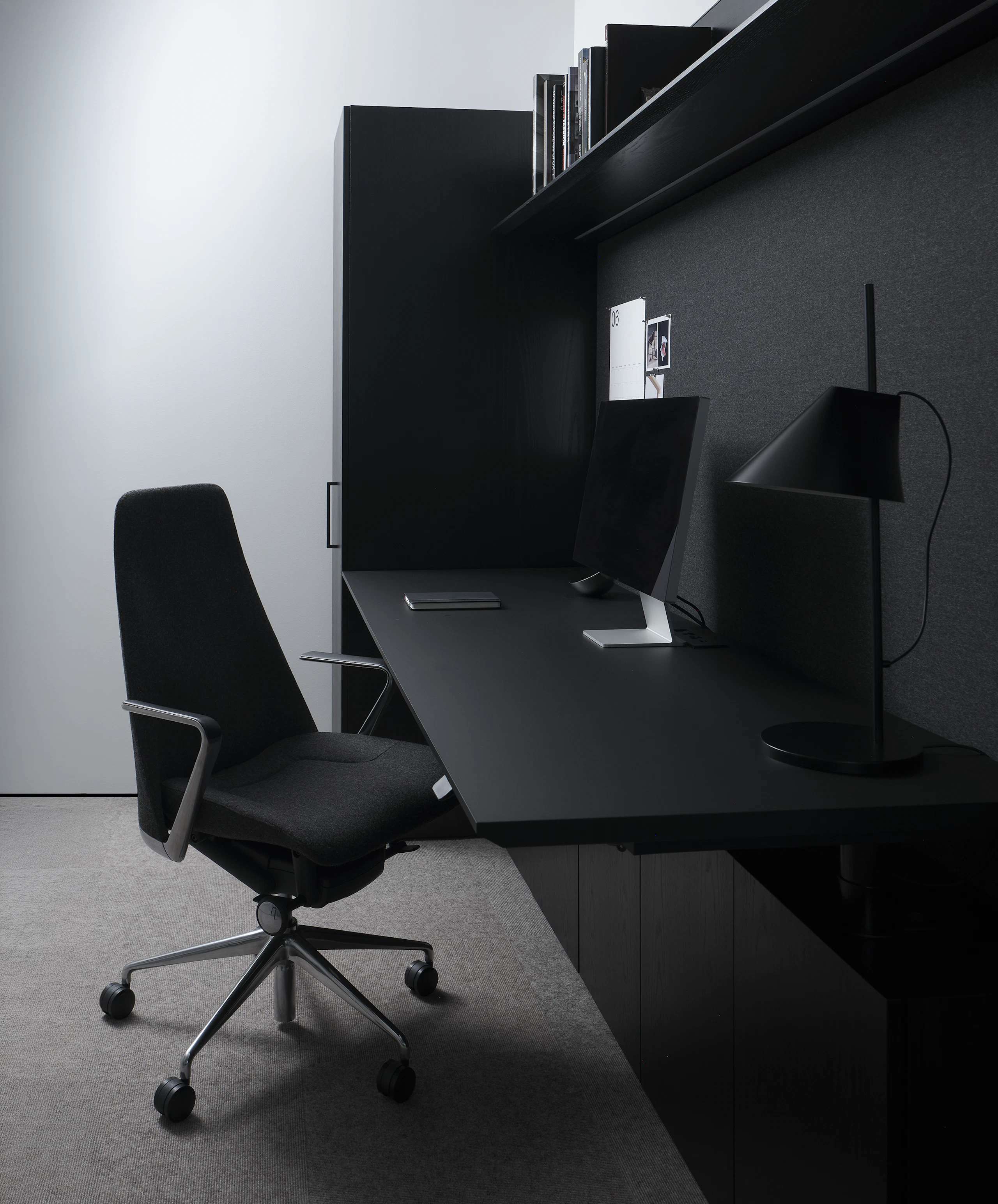 Geiger One Private Office in Ebonized Flat Cut Ash with a black soft-touch laminate height-adjustable work surface and Taper Chair, viewed from the side.