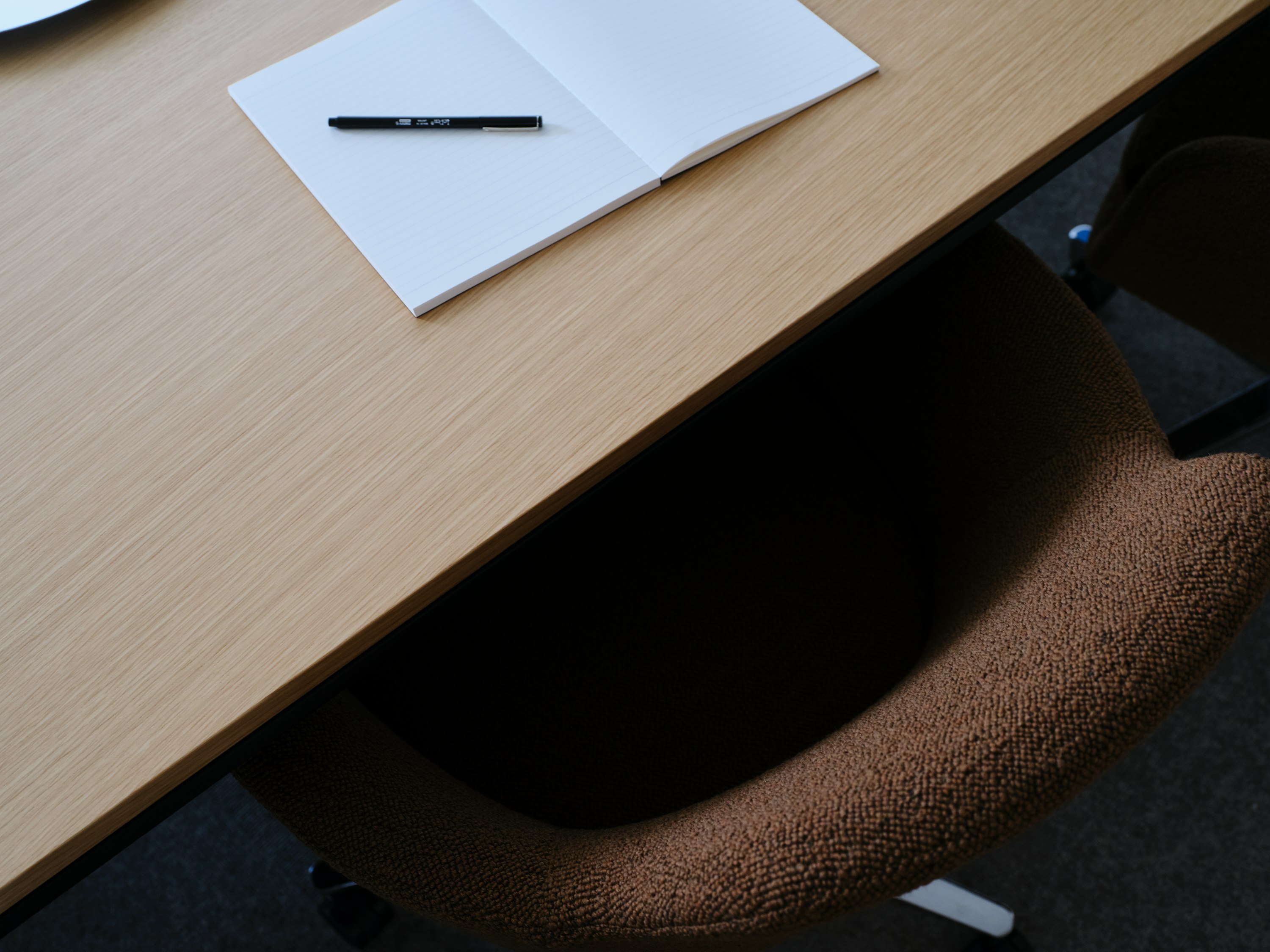 Detail view of the Ascent Conference Table designed by EOOS in Natural Rift Cut Oak with a Saiba chair upholstered in a brown textile, viewed from above at an angle.