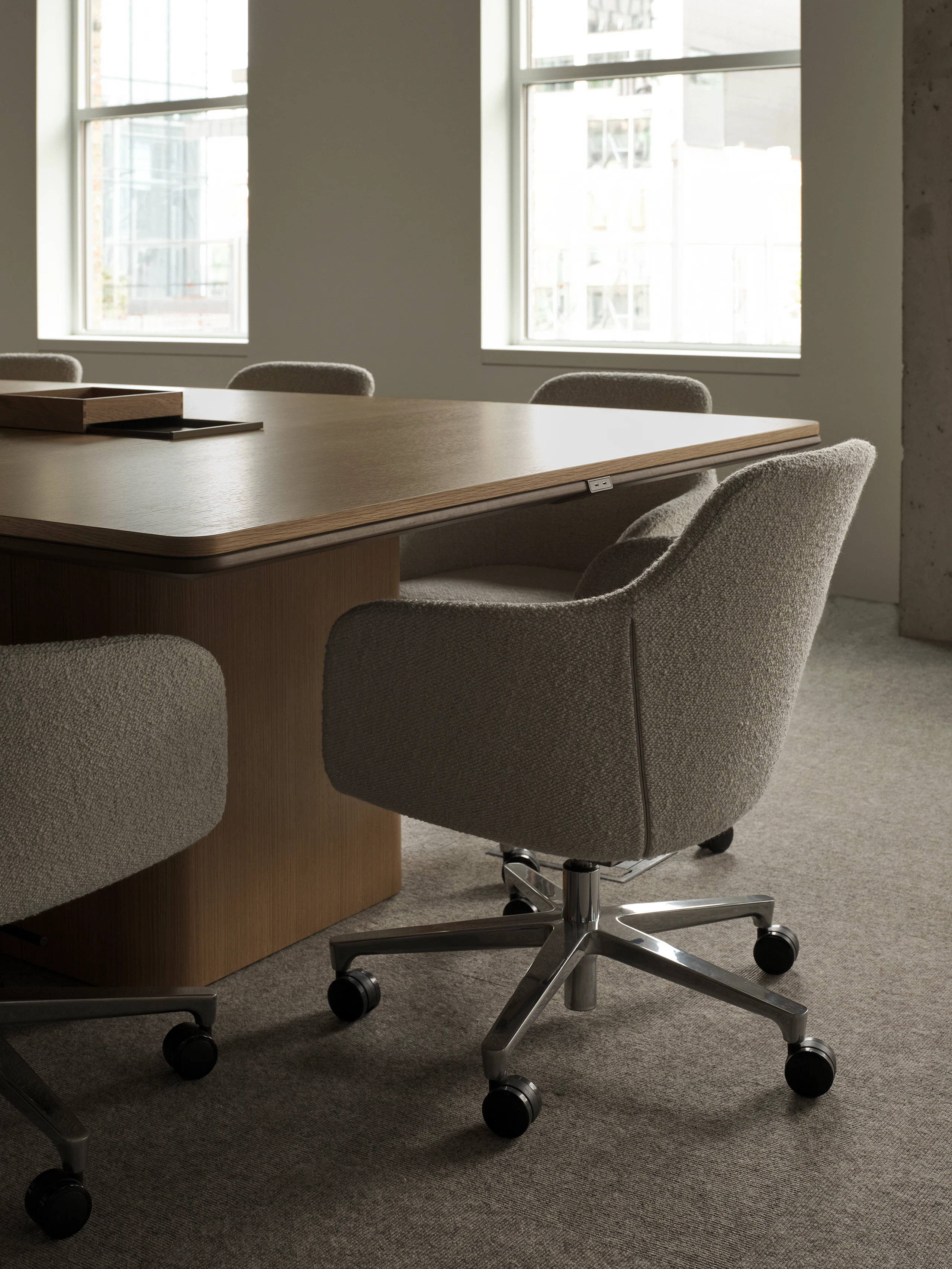 An Ascent Conference Table in Natural Rift Cut Oak with a plinth base surrounded by Saiba Conference Chairs upholstered with Pristina in Dove, viewed at an angle.