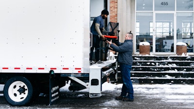 Two people loading a Sayl Chair by Herman Miller into a white delivery truck.