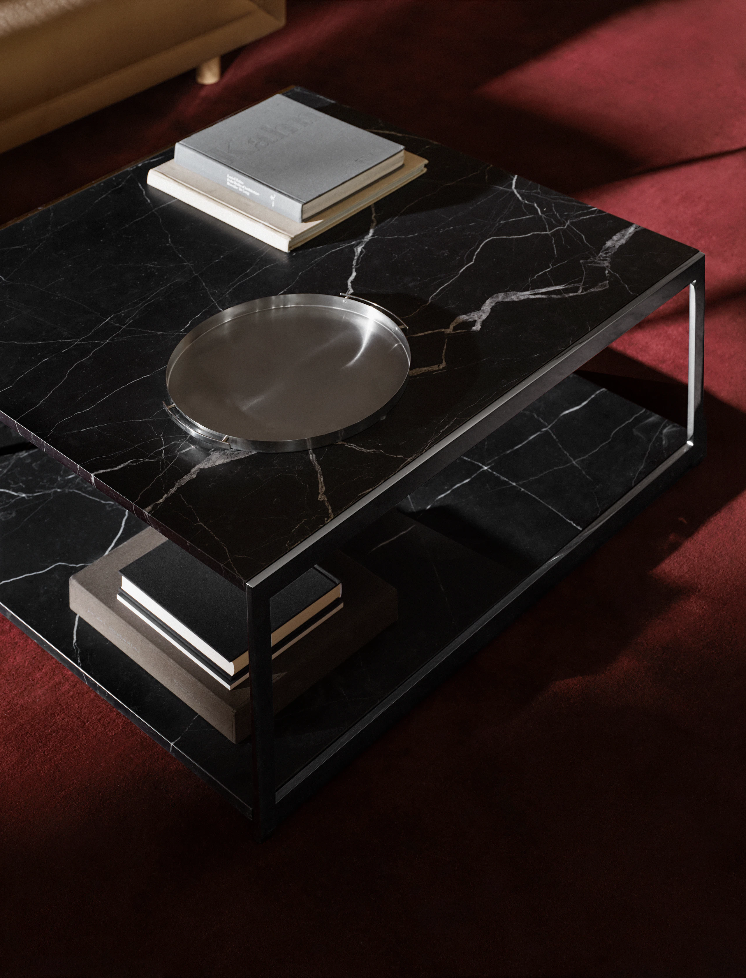 H Frame Coffee Table with a Nero Marquina Marble top and bottom and chrome frame, styled with books and a metal platter, viewed from above at an angle on a burgundy rug.