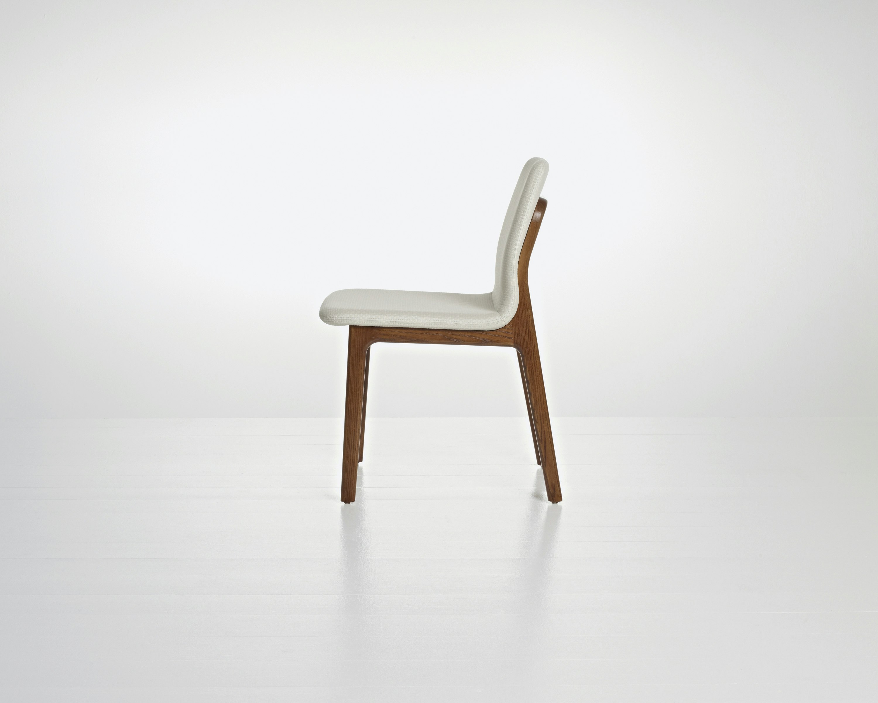 Side view of a Deft side chair with ivory-colored fabric, a wood frame in a medium finish, and no arms.