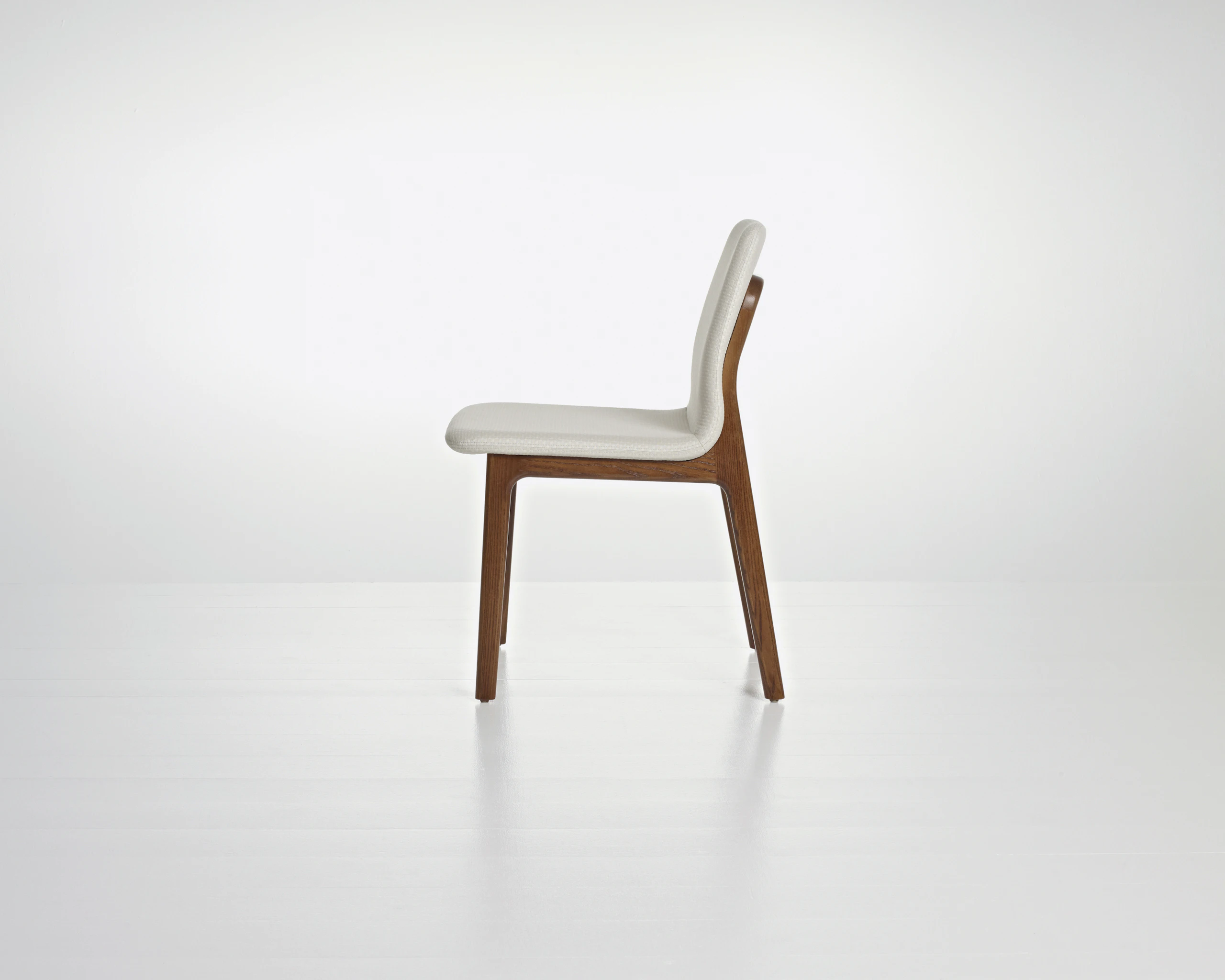 Side view of a Deft side chair with ivory-colored fabric, a wood frame in a medium finish, and no arms.