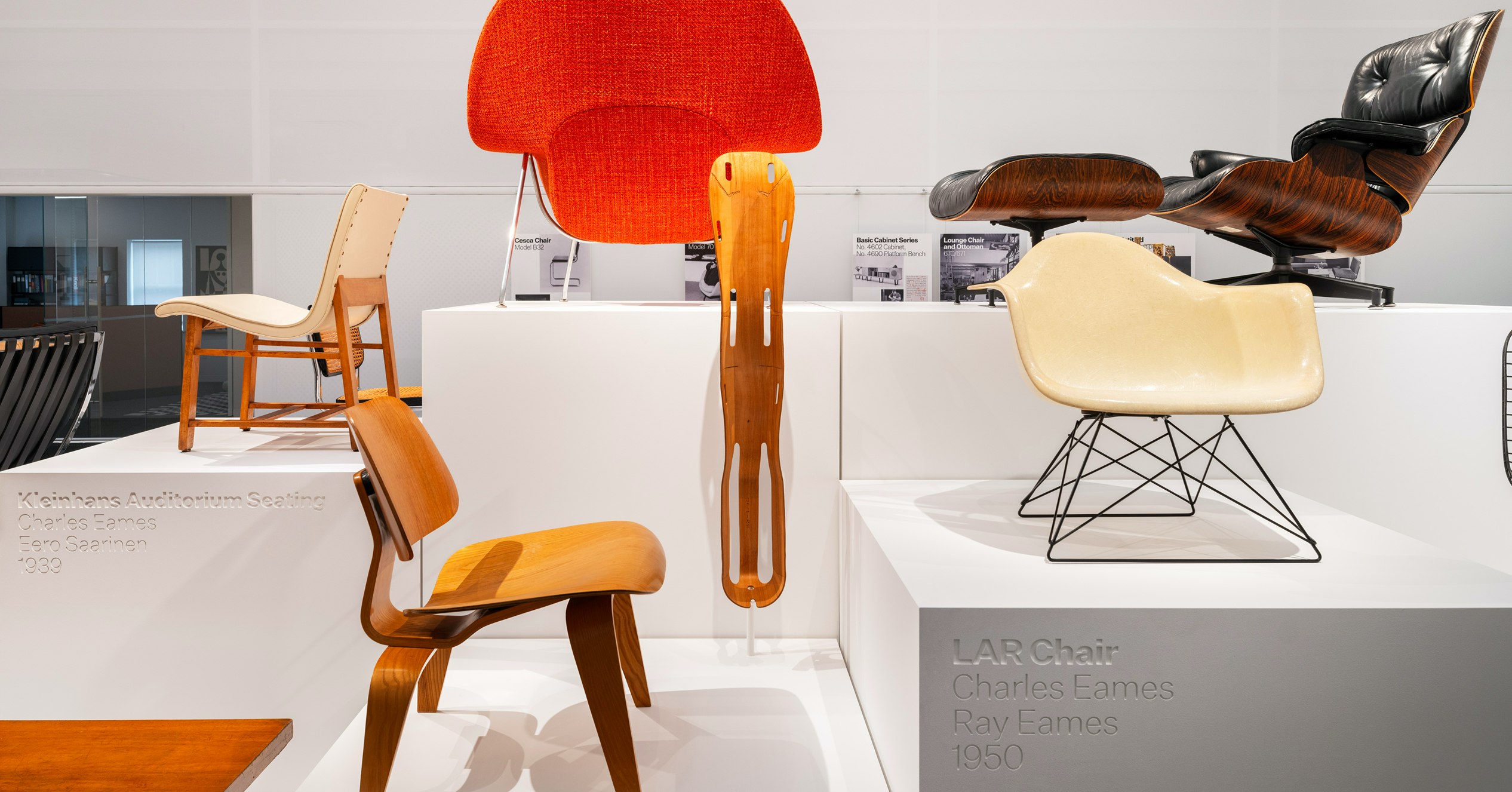 An LAR Chair, Eames Lounge Chair and Ottoman, Knoll Womb Chair and others on white pedestals on display at the MillerKnoll Archives
