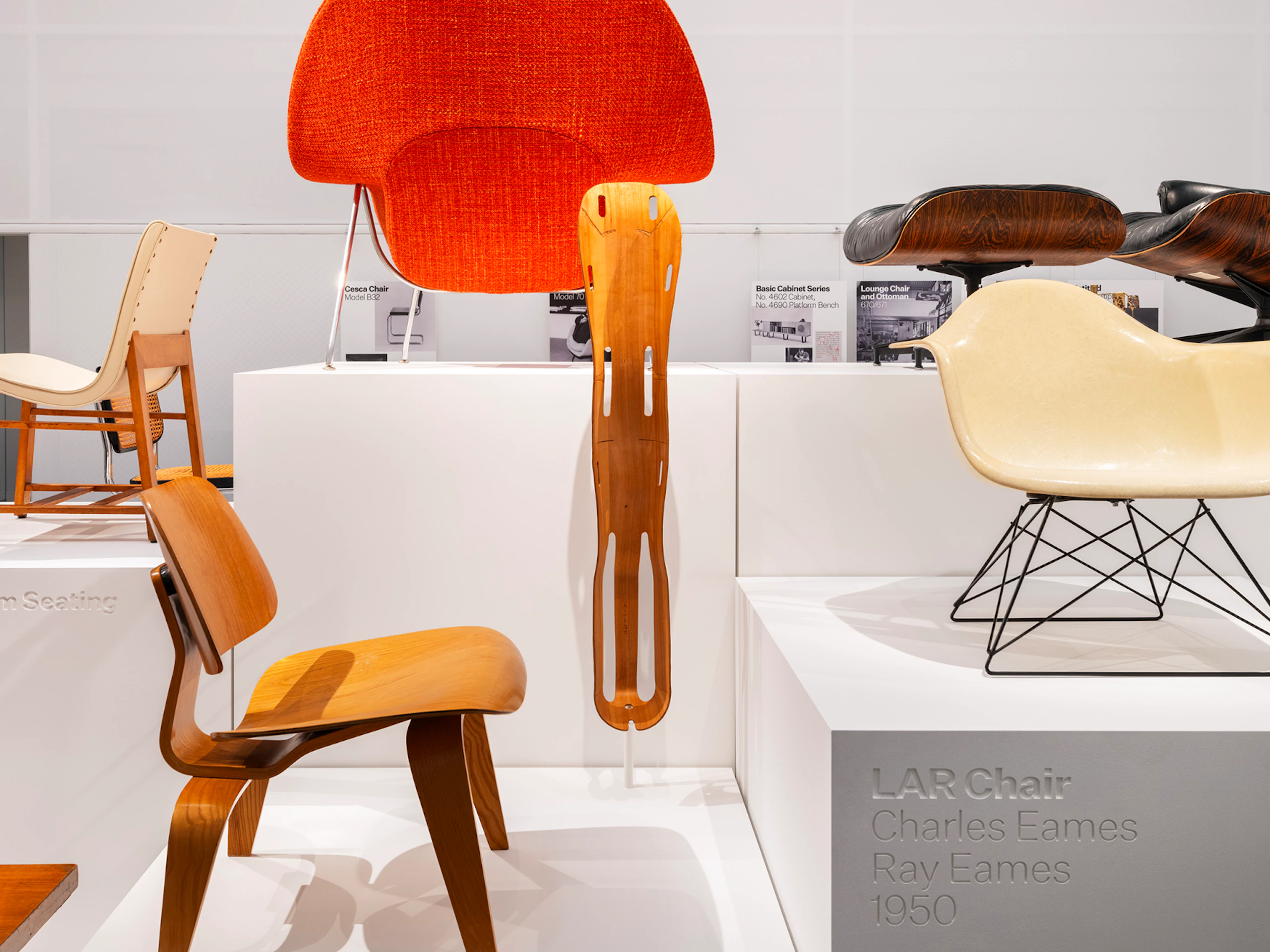 An LAR Chair, Eames Lounge Chair and Ottoman, Knoll Womb Chair and others on white pedestals on display at the MillerKnoll Archives
