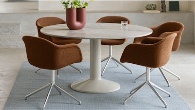 Four brown task chairs placed around a round white Midst Marble table from Muuto