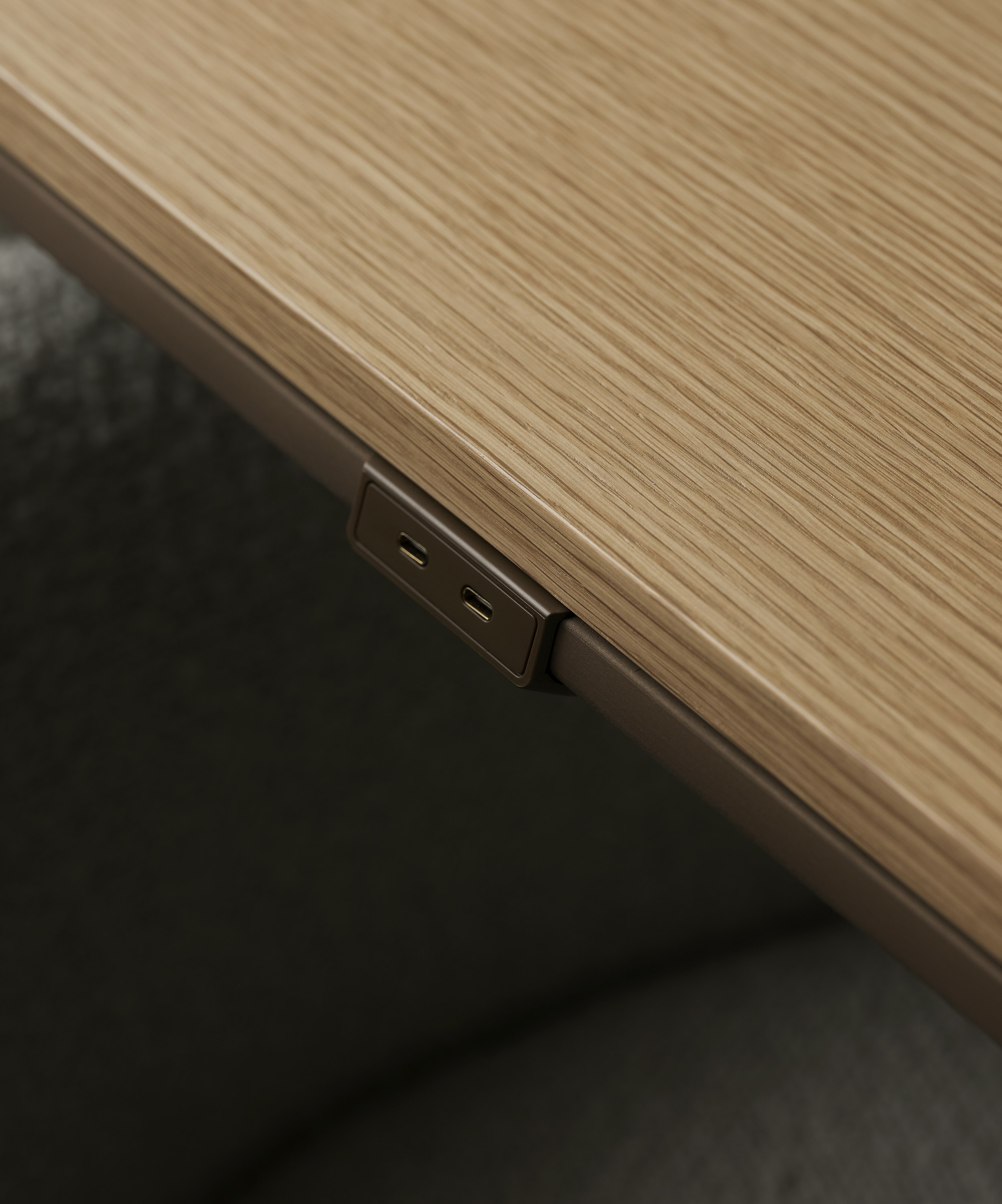 Detail view of the Ascent Conference Table perimeter power in luxe medium bronze with a Natural Rift Cut Oak tabletop, viewed from above at an angle.