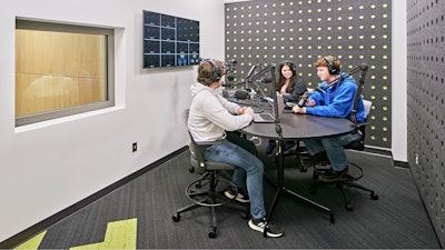 Three students sitting around a table and using recording equipment in an audio recording booth