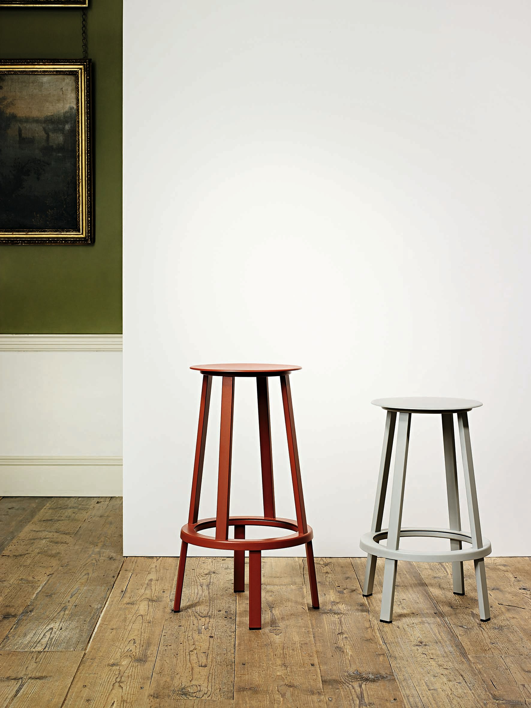 Red and grey Revolver Stools with two different heights standing next to eachother against a wall.