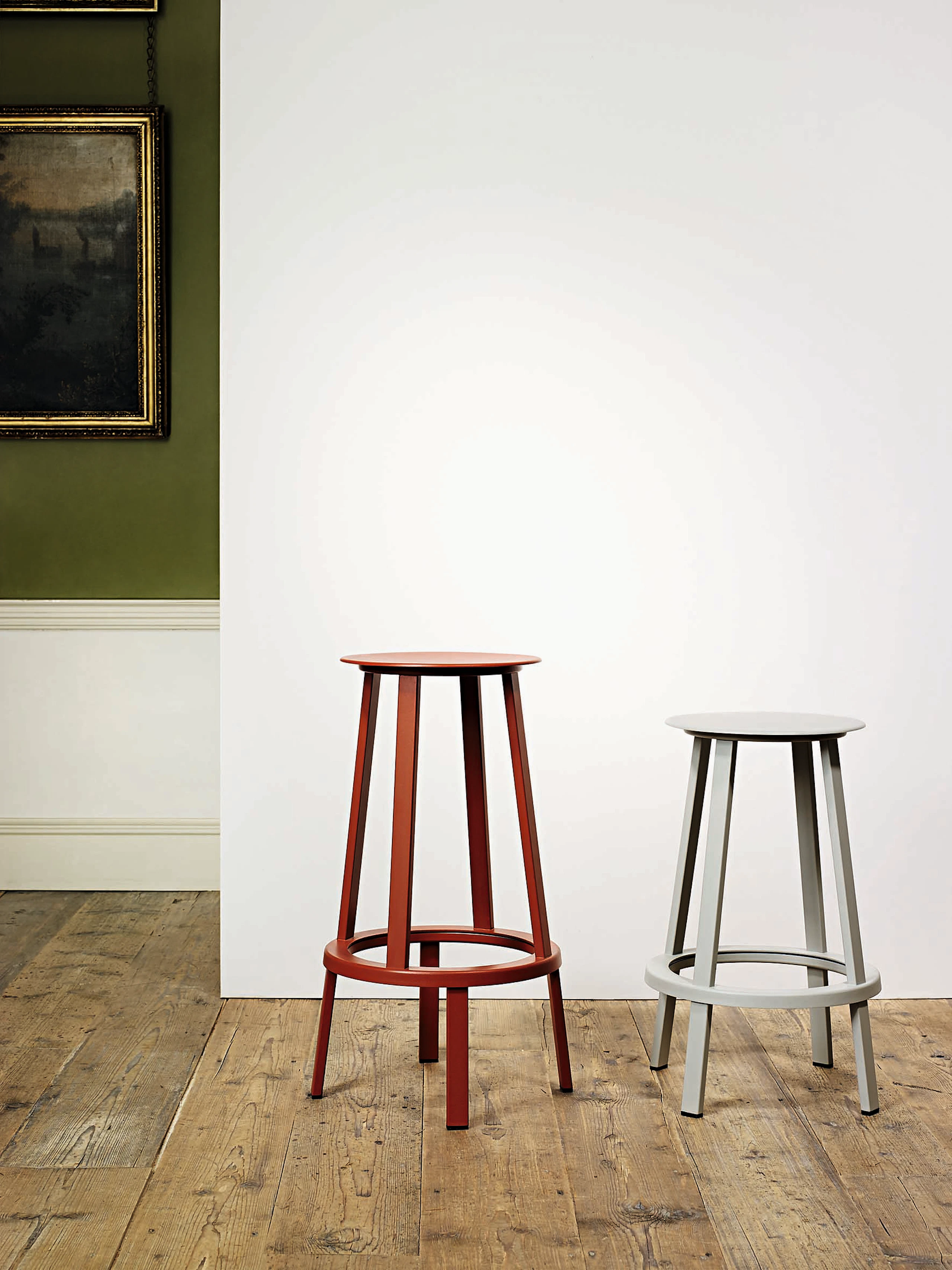 Red and grey Revolver Stools with two different heights standing next to eachother against a wall.