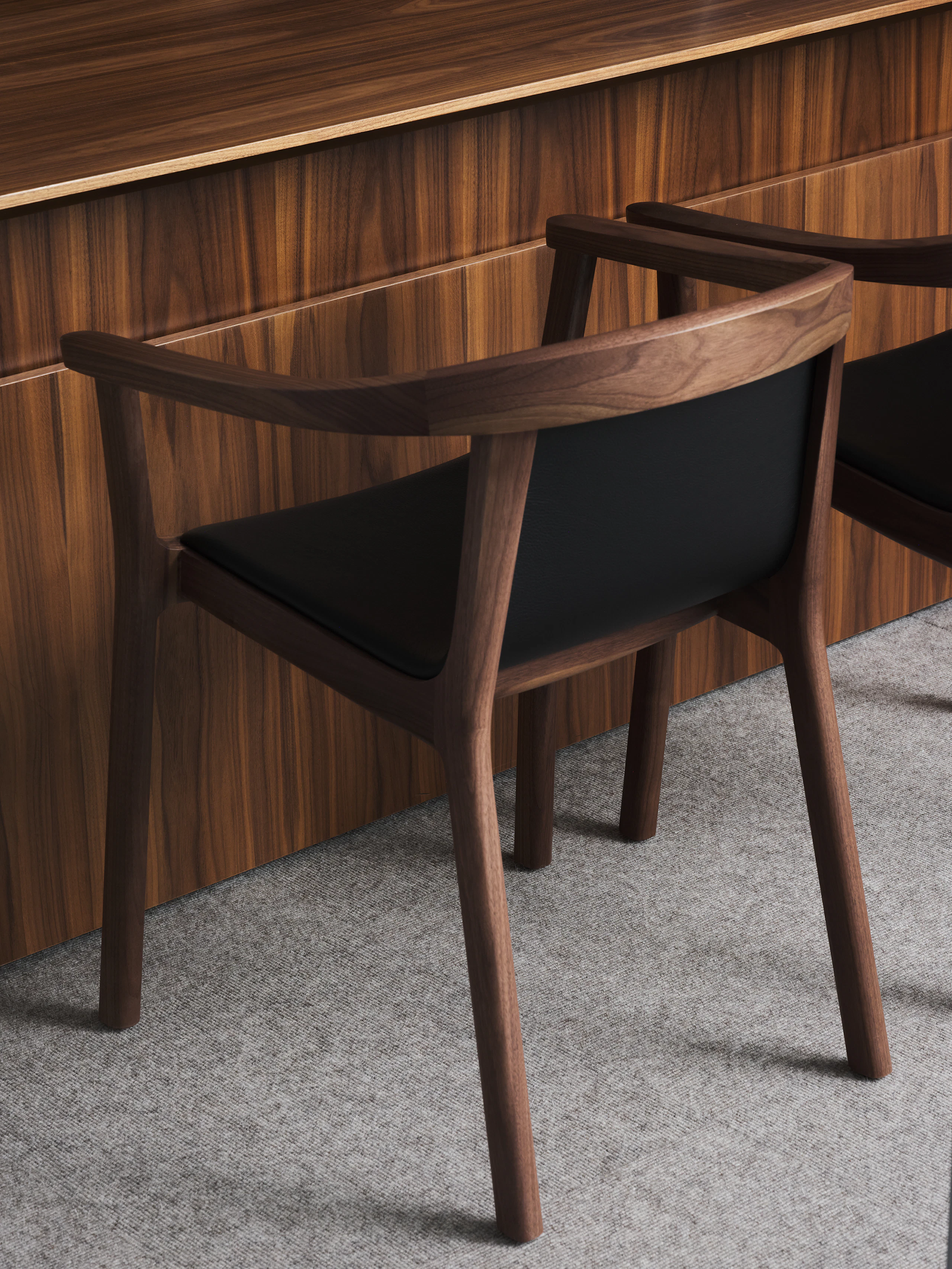 Two Lijn Armchairs in Natural Walnut upholstered with Prone Leather in Obsidian, viewed from behind at an angle in a Geiger One Private Office.
