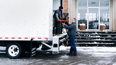Two people loading a Sayl Chair by Herman Miller into a white delivery truck.