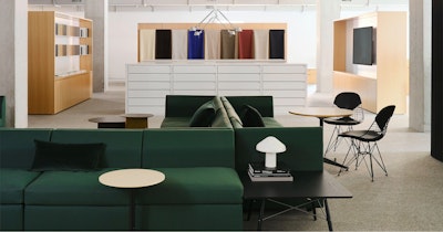 Several large green sofas and black side tables with a large showroom with textiles in a variety of colors lining the walls in the background at the MillerKnoll showroom at Design Days