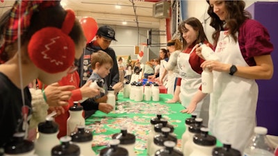 A table of volunteers at a We Care event talking with several children. Water bottles and stickers can be seen on a green table.