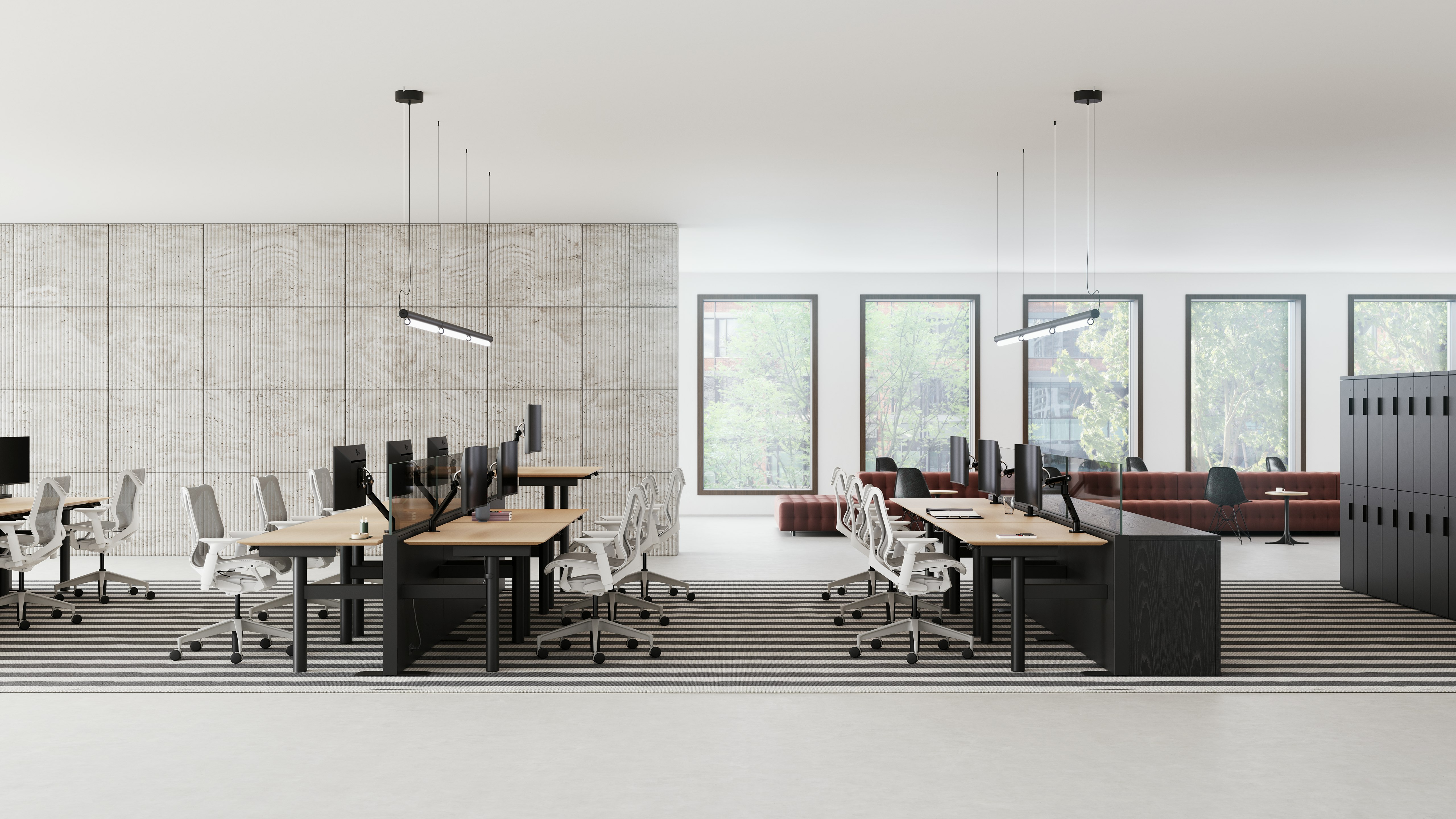 An open office that has benching style workstations in rows, with casual collaborative spaces in the background.