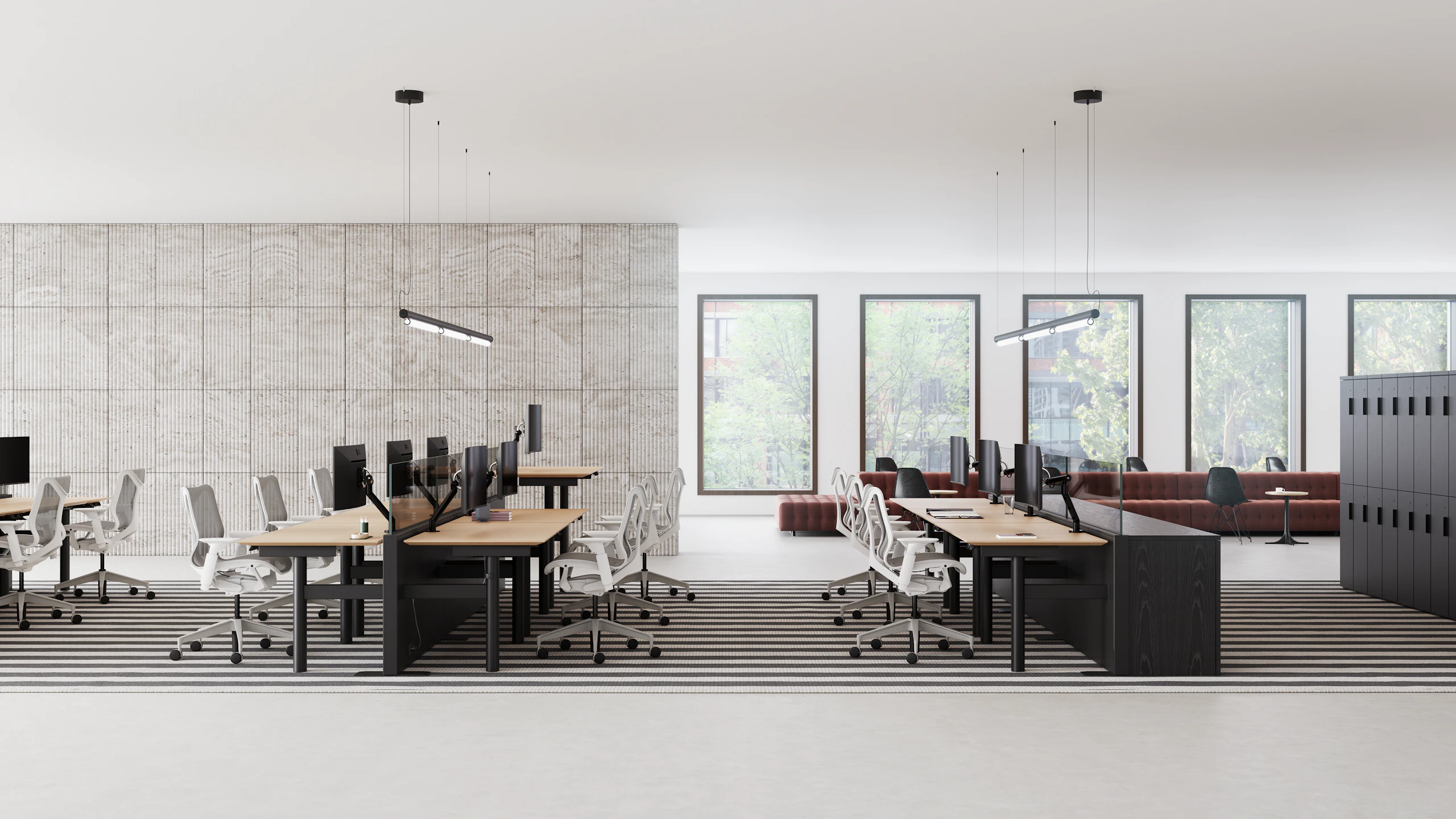 An open office that has benching style workstations in rows, with casual collaborative spaces in the background.
