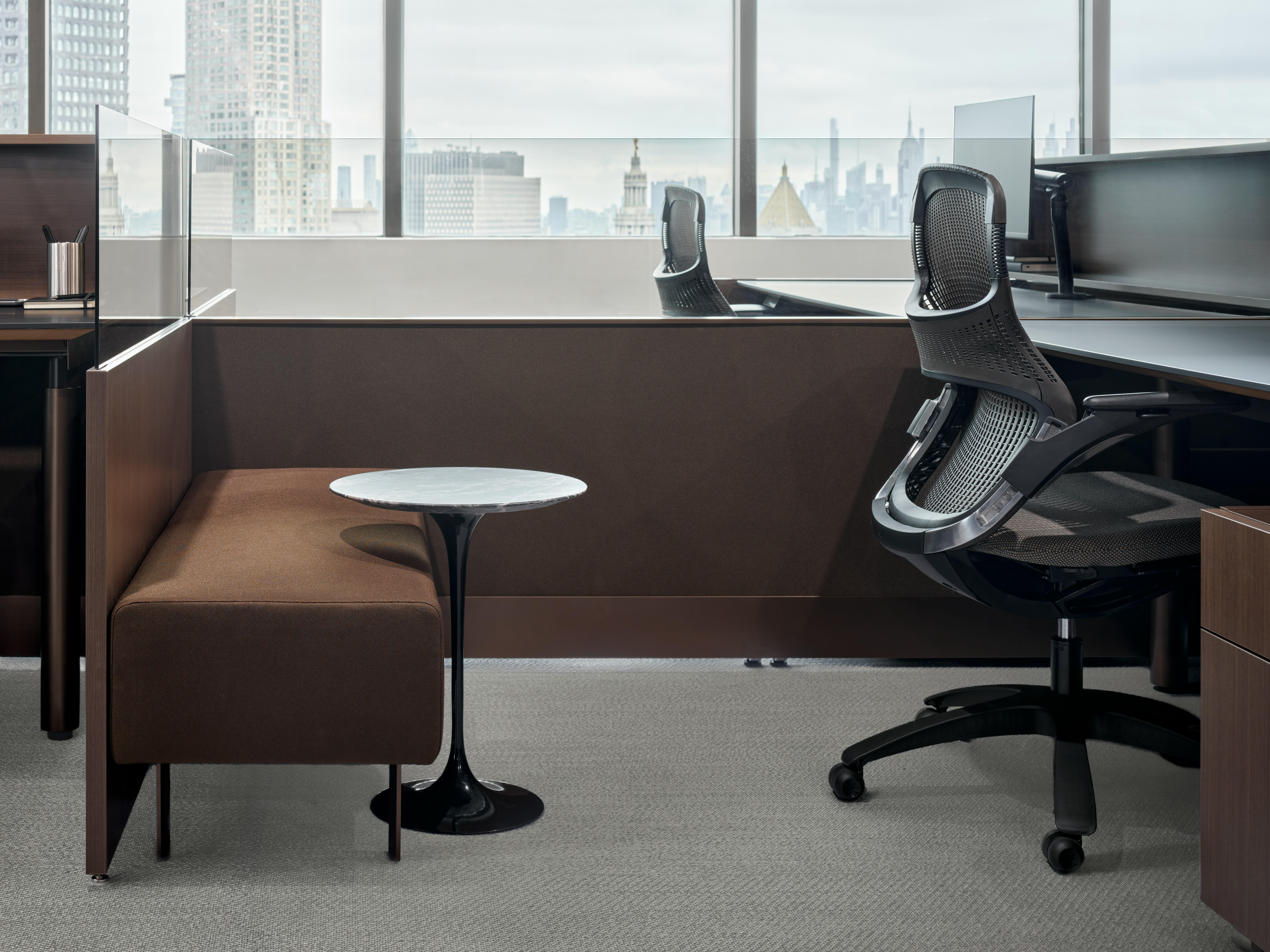 A workstation with a personal storage pedestal, a bench and small side table, and a work chair and height adjustable desk are viewed from the side.