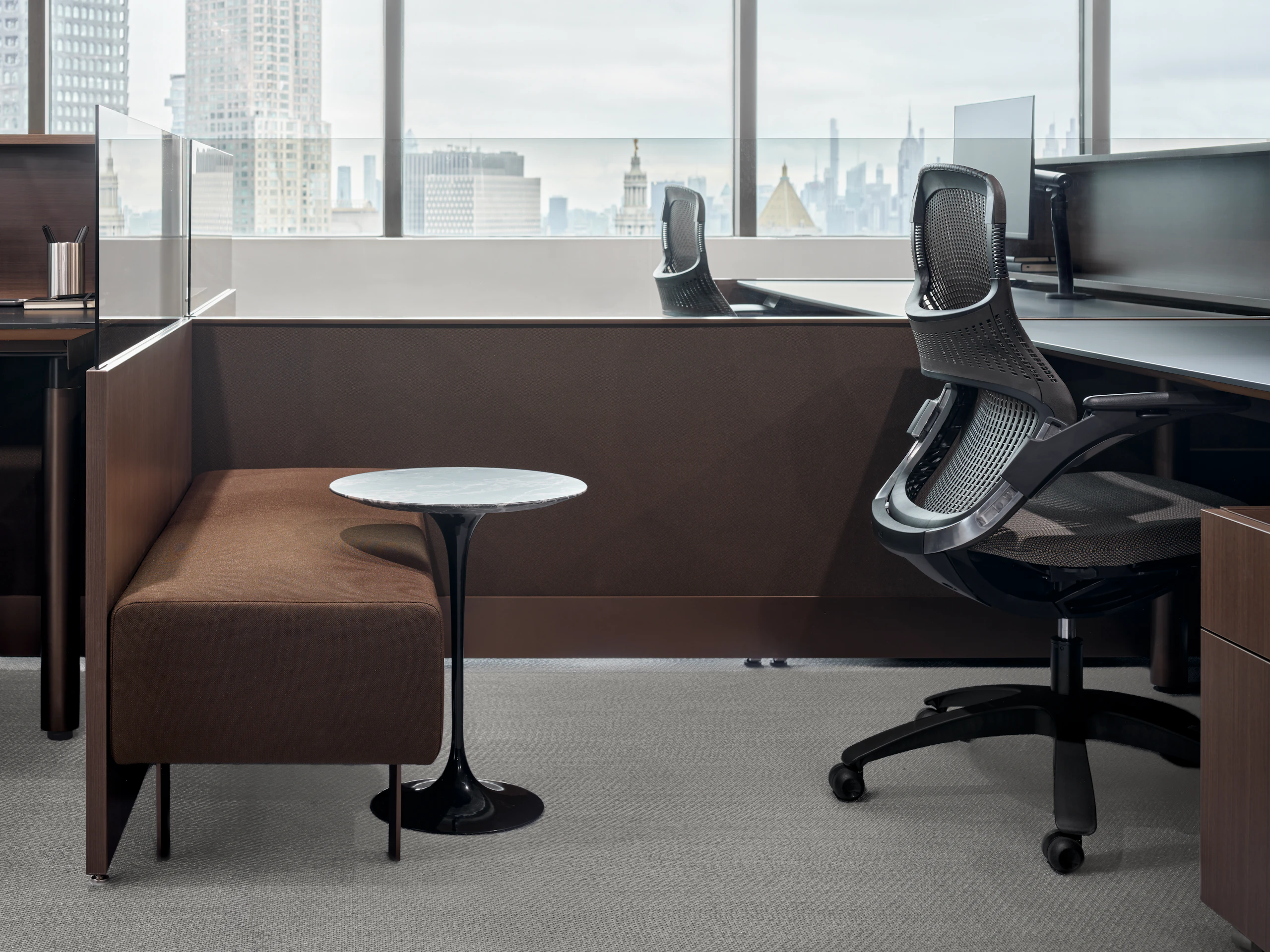 A workstation with a personal storage pedestal, a bench and small side table, and a work chair and height adjustable desk are viewed from the side.