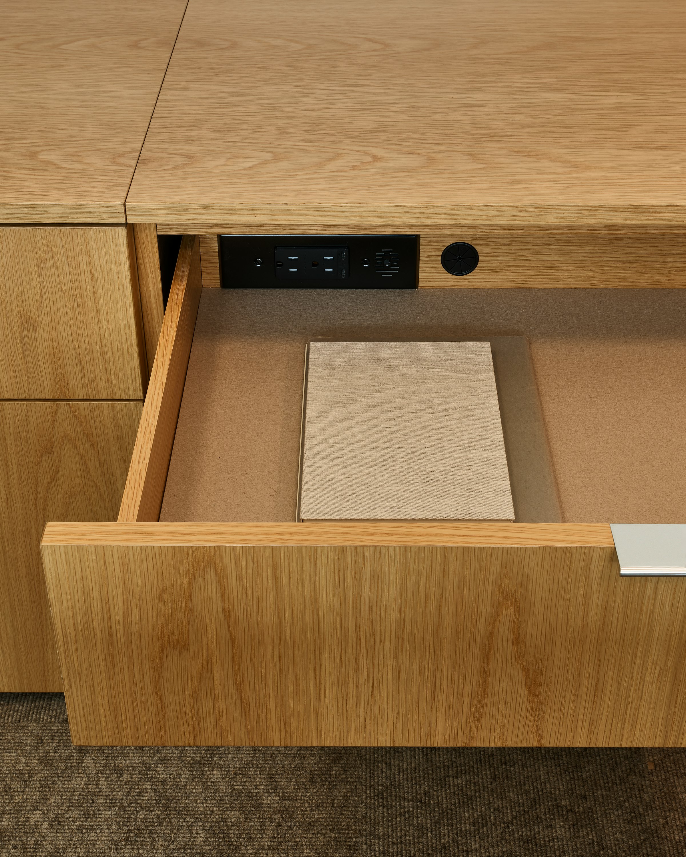Detail view of a Geiger One Casegoods Private Office open storage drawer in Natural Flat Cut Oak with in-drawer power, viewed from the front in a private office setting.