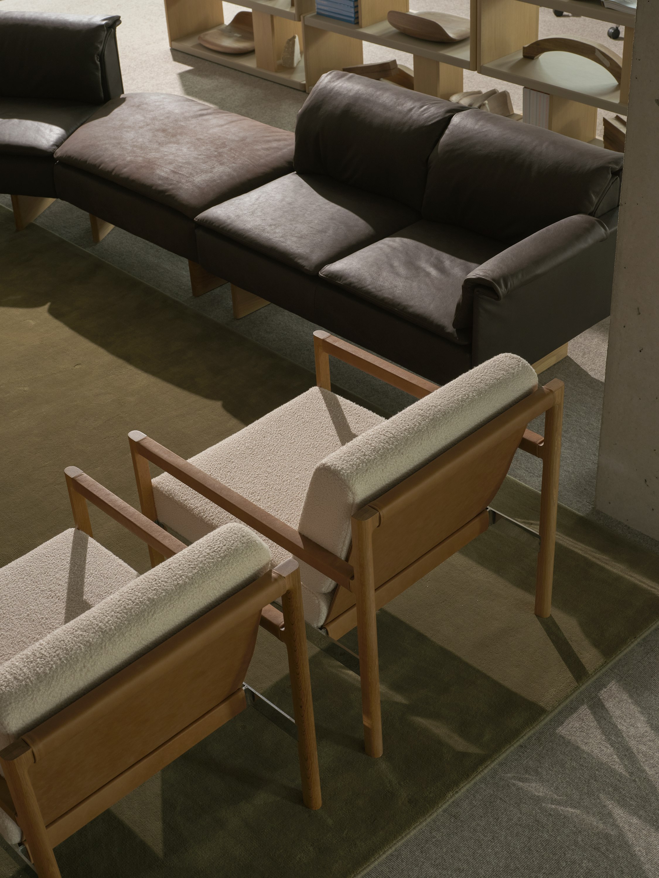 Detail view of the backs of two Brabo Club Chairs with Natural Oak and chrome frames and upholstered with Maharam Firth in Limewash and a Mantle Sectional Sofa and New Canaan Bookshelf in the background, viewed from above at an angle.