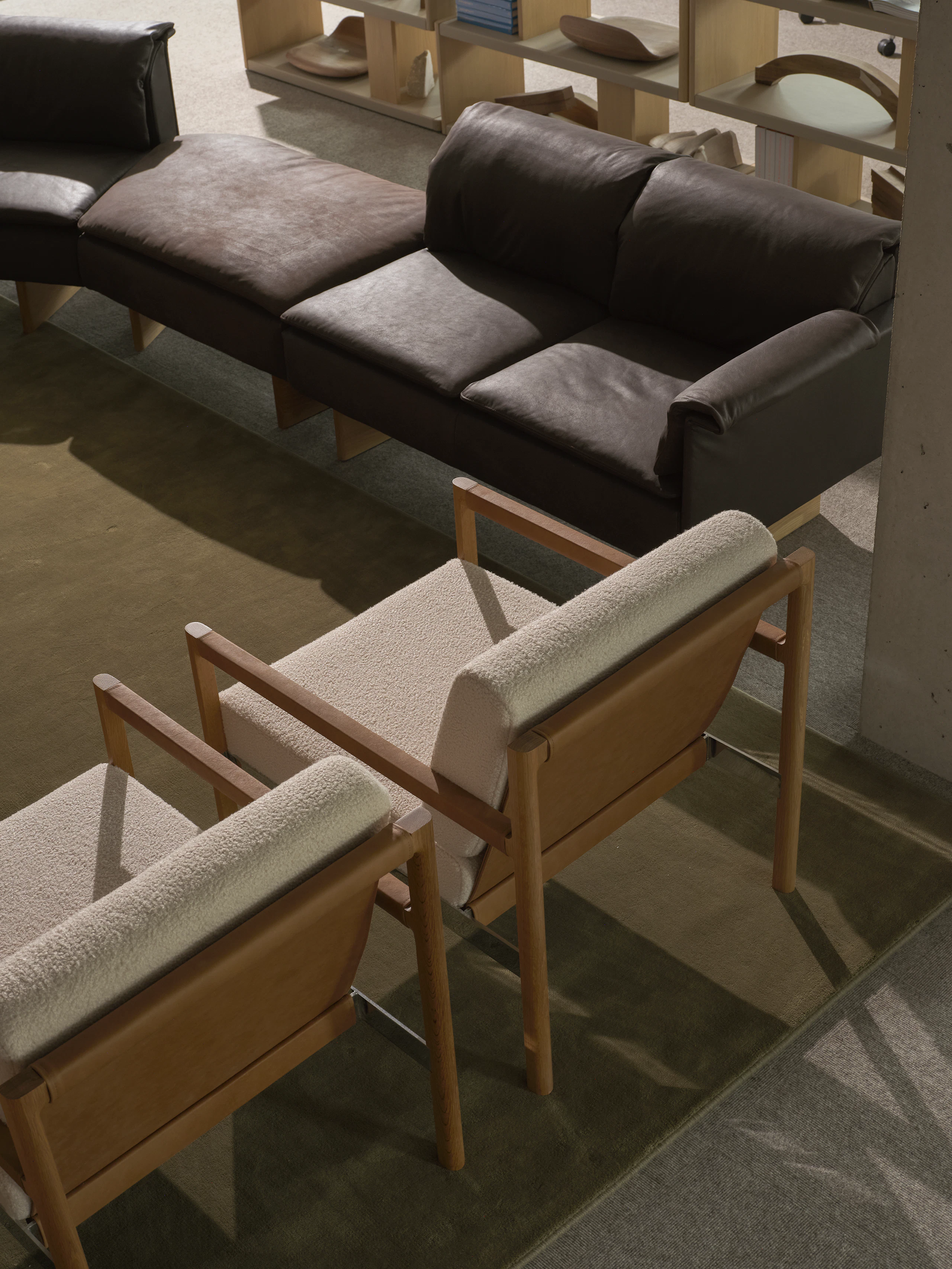 Detail view of the backs of two Brabo Club Chairs with Natural Oak and chrome frames and upholstered with Maharam Firth in Limewash and a Mantle Sectional Sofa and New Canaan Bookshelf in the background, viewed from above at an angle.