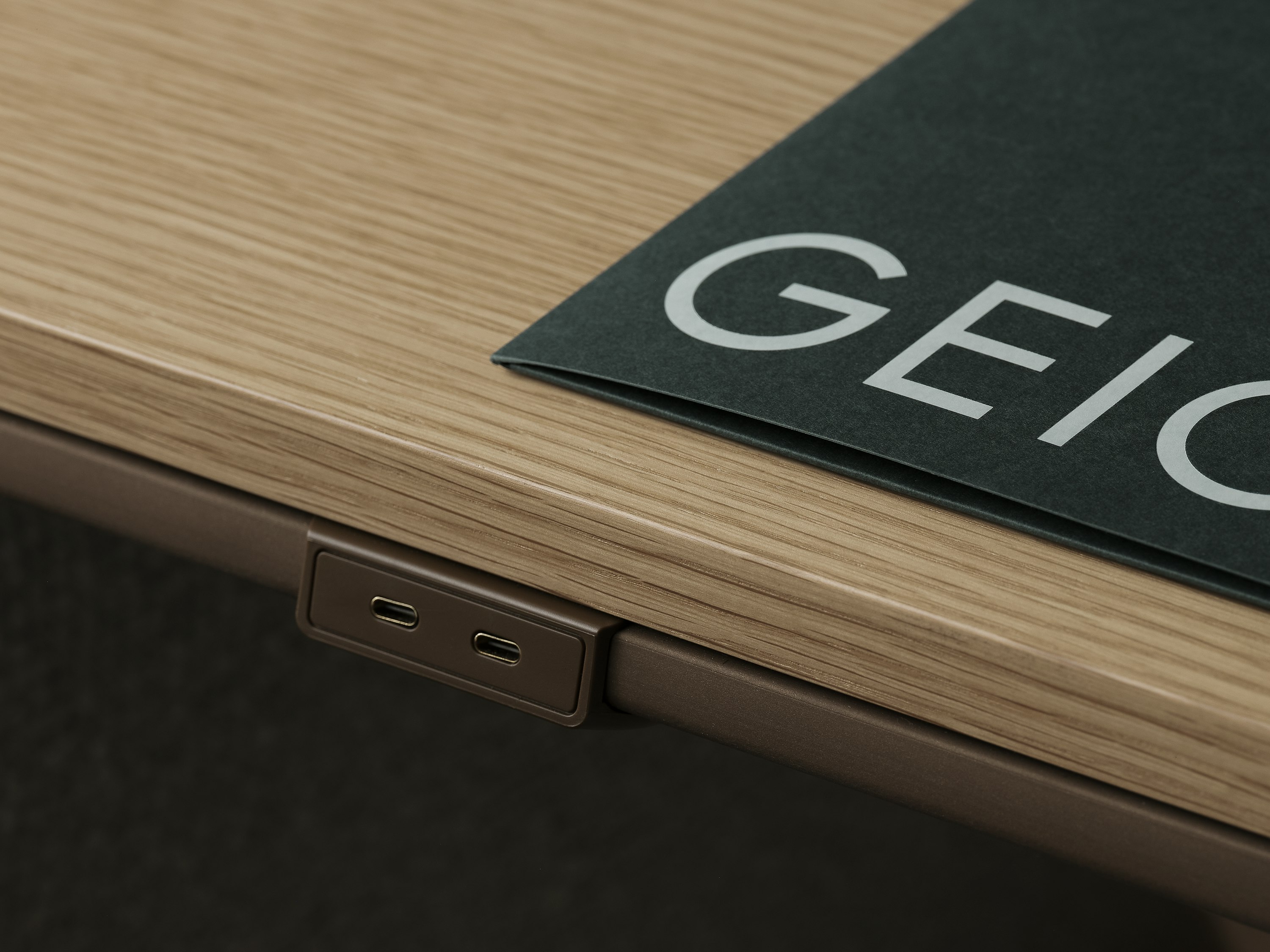 Detail view of the Ascent Conference Table perimeter power in luxe medium bronze with a Natural Rift Cut Oak tabletop and a Geiger presentation folder on top, viewed at an angle.