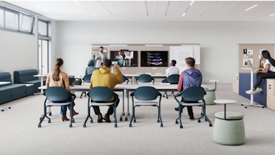 Aula moderna con foco en la colaboración. En primer plano se ve una larga mesa blanca con computadoras portátiles. El fondo muestra cabinas cerradas con paneles de tela roja y marcos blancos, algunas con asientos y pequeñas mesas en el interior.