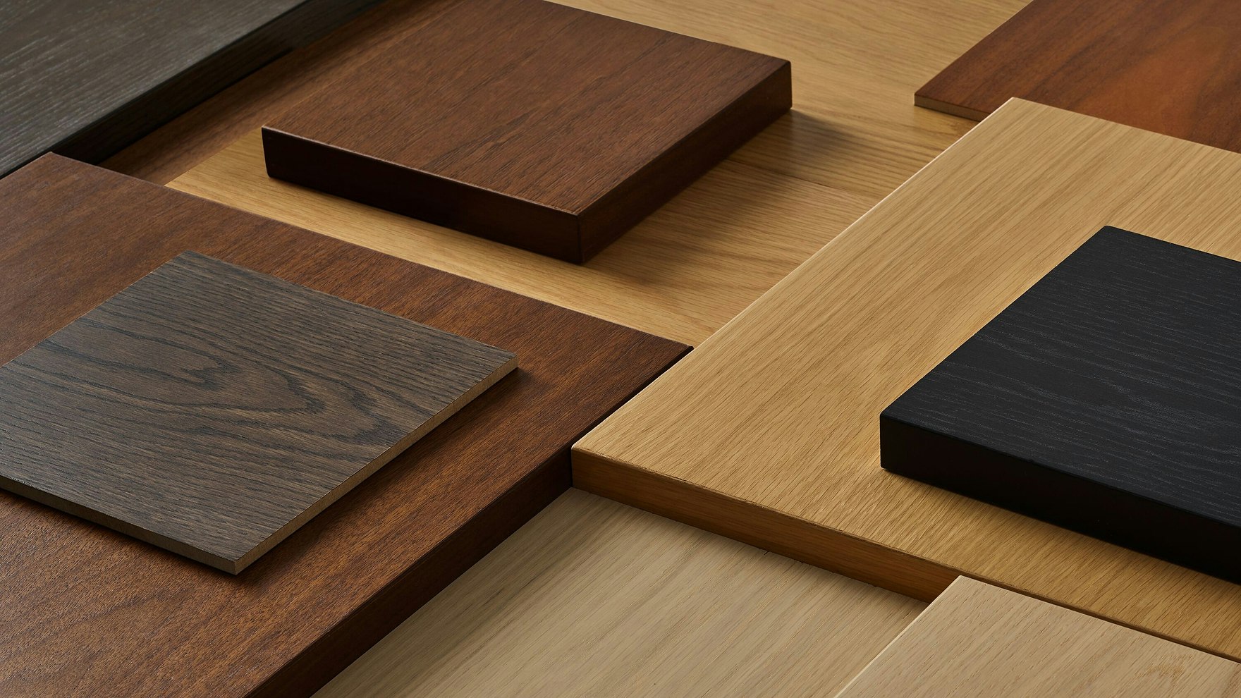 A collection of square pieces of wood and veneer finishes from the MillerKnoll Central Palette ranging in color from black, dark brown, and light brown.