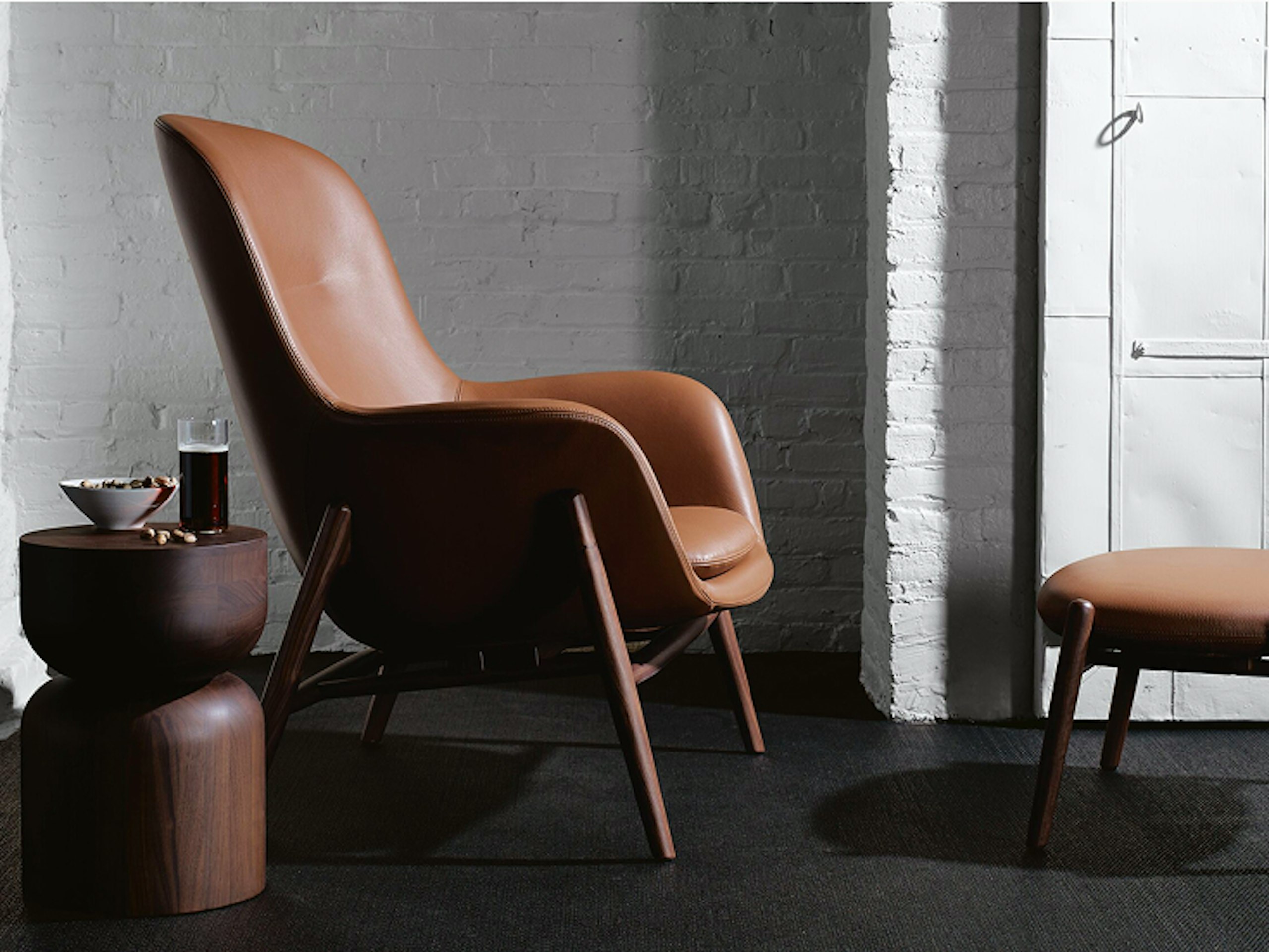 A brown Nora Lounge Chair and Ottoman from the DWR Collection