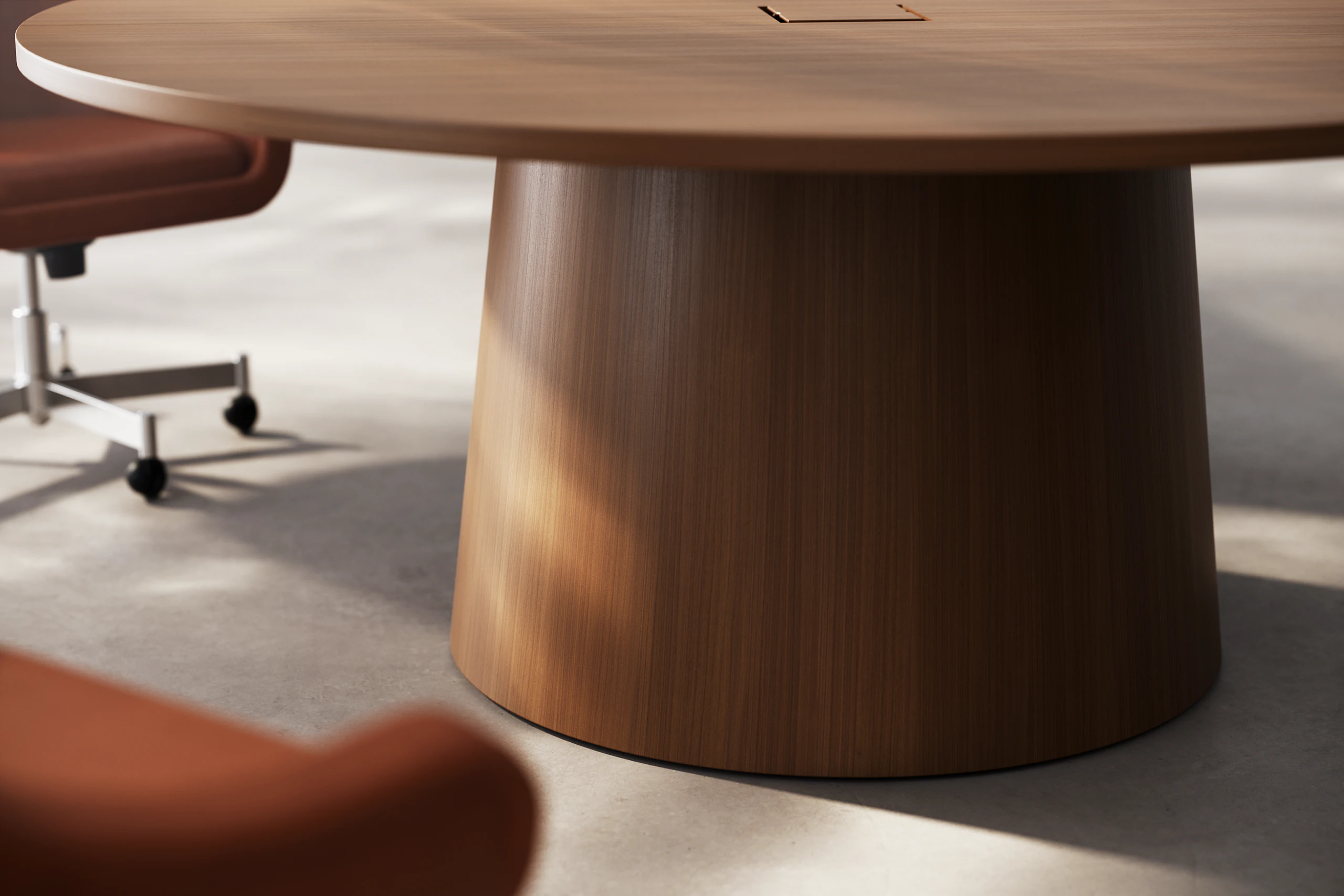 Detail of JD Meeting Table showing tapered round base in natural quarter cut walnut with two bumper chairs on a concrete floor.