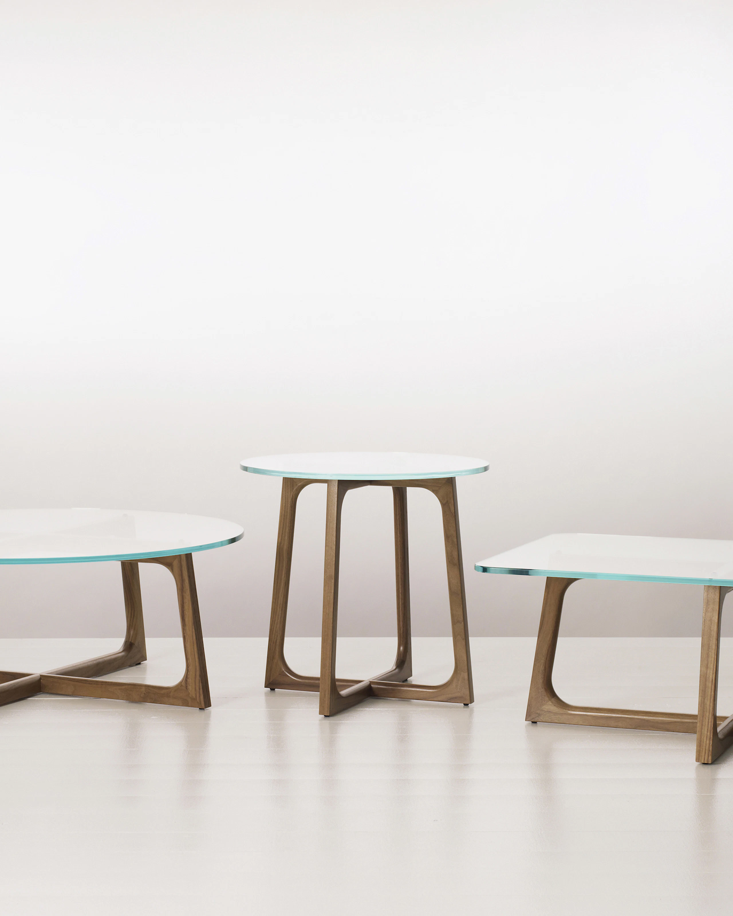 Three Loophole occasional tables of different sizes and shapes, each with a glass top and walnut base.