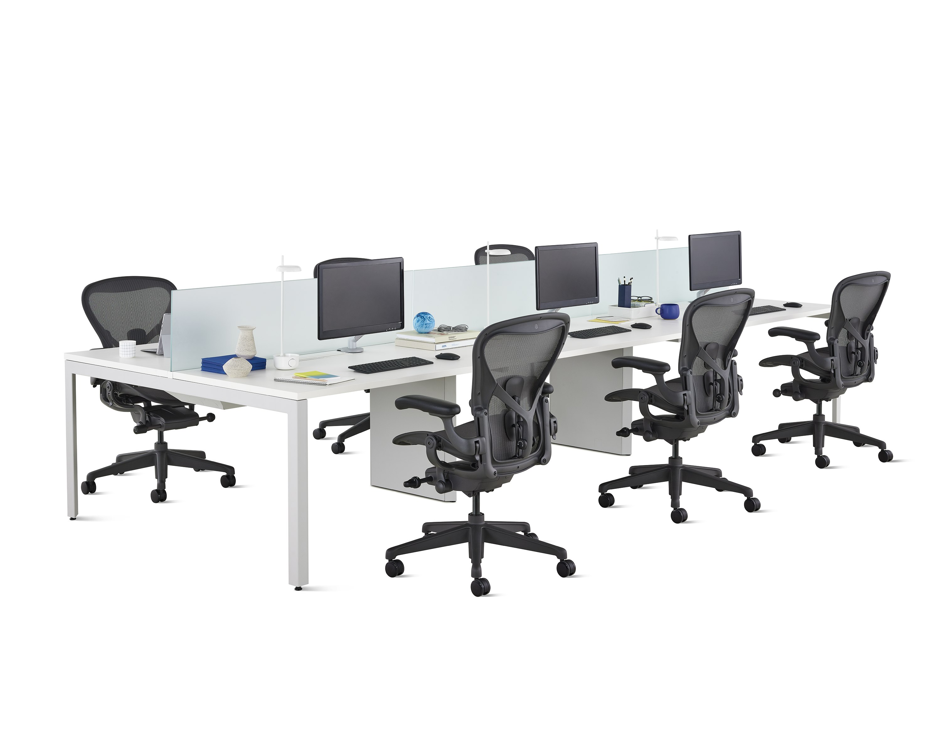 A white Layout Studio benching workstation for six with frosted glass center privacy screens, desk accessories, and six black Aeron Chairs.