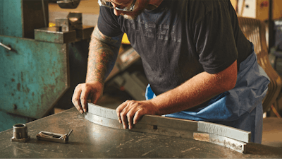 A man wearing safety glasses placing two curved pieces of metal atop eachother on a worktable in an industrial environment.