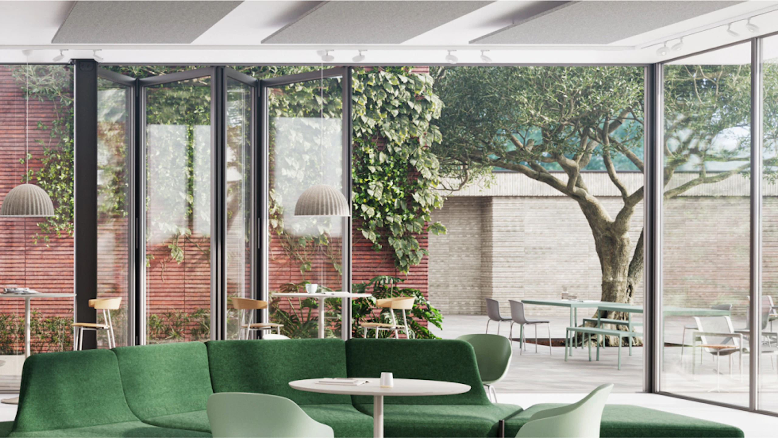 Lounge with green sofa and light chairs, overlooking outdoor patio through large glass doors. Patio features tables, chairs, and lush greenery including a large tree.