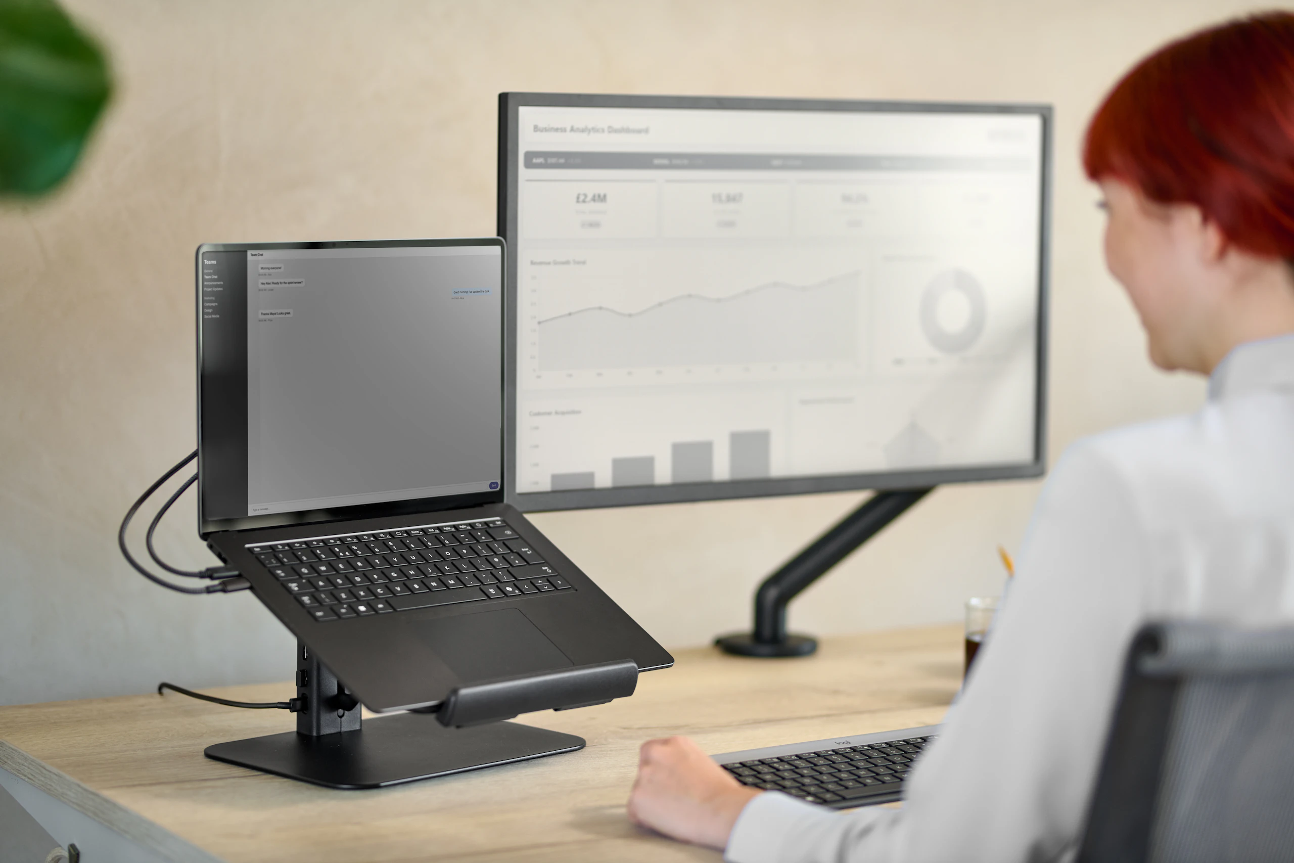 Person with red hair using black Lana laptop stand and Flo monitor arm in a working environment.