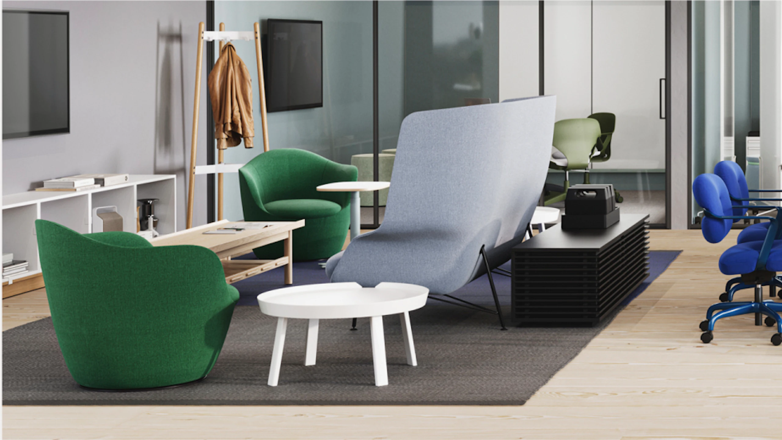 Modern lounge area with green and grey armchairs, a small white table, and a black storage unit. A coat rack with jackets stands nearby. Large windows and a glass-walled office in the background.