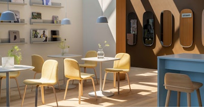 A brightly lit cafe setting furnished with Muuto furniture at MillerKnoll Design Days. Yellow chairs are arranged around small white tables with a row of wall mirrors in the background.