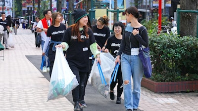 A group of people wearing black MillerKnoll shirts, carrying rubbish bags as they walk along a sidewalk.