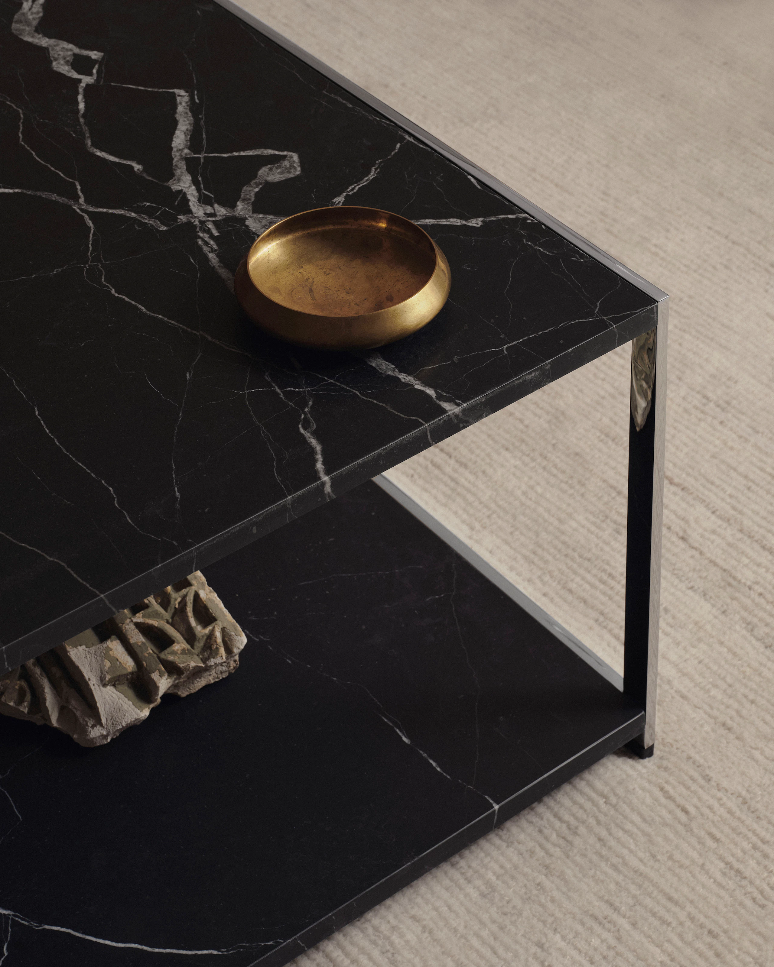 Detail view of an H Frame Coffee Table with a Nero Marquina Marble top and bottom and chrome frame, styled metal platter, viewed from above at an angle on a beige rug.