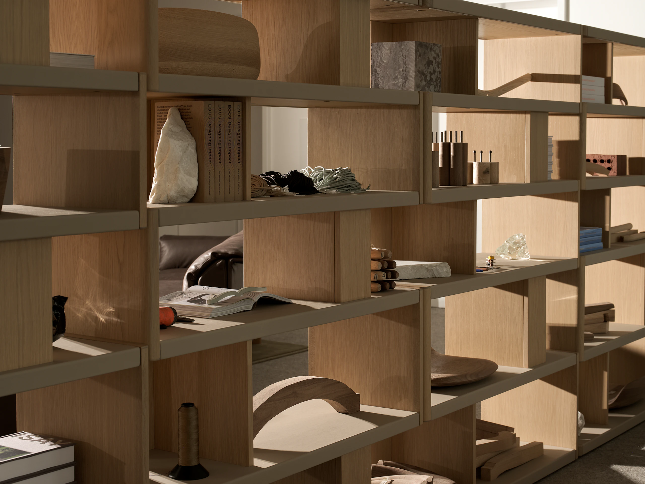 Various New Canaan Tall Bookshelves in Light Oak wrapped with Bristol Leather in Champagne arranged side by side and styled with various objects, viewed at an angle.