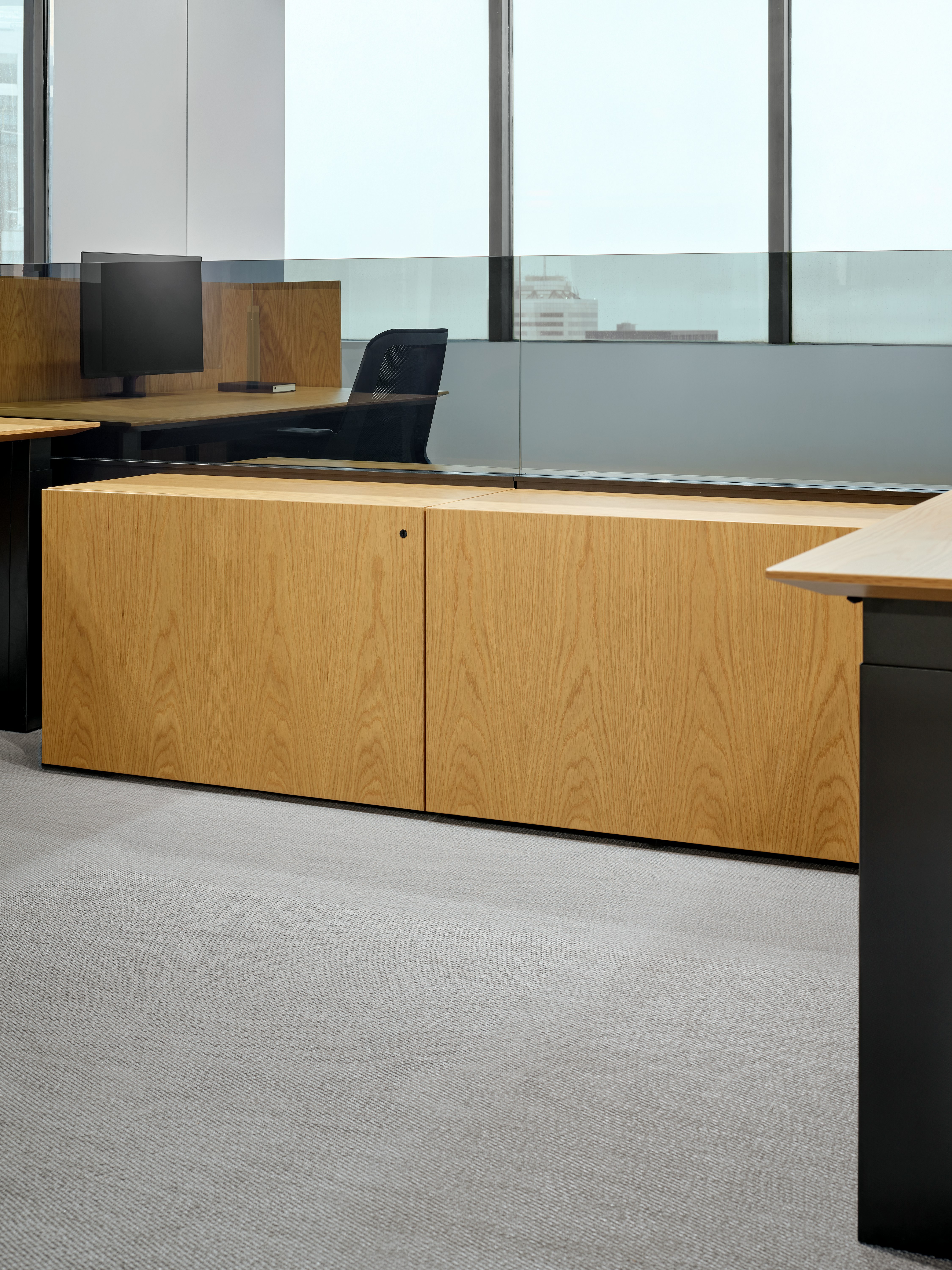 A detail view of storage credenzas between workstations also shows a workstation and work chair behind a glass add up in the background.