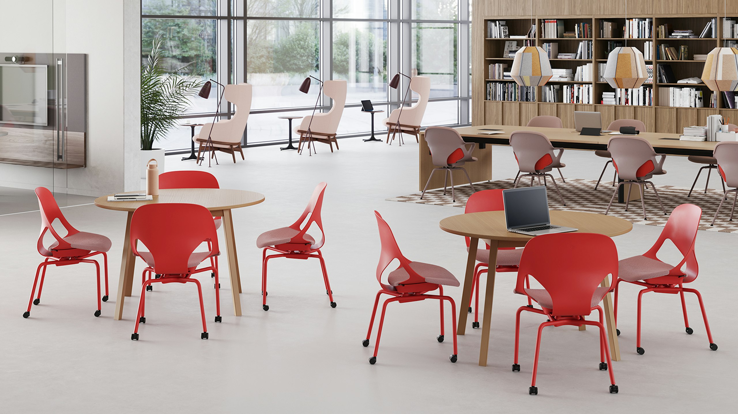 Two round table each with four red Zeph side chairs are in front of a long rectangular project table with eight red Zeph side chairs with light brown knit covers in a common area.