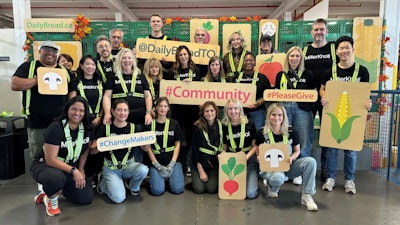 A group of MillerKnoll associates who volunteered at the Daily Bread Food Bank holding wood signs that show images of food.