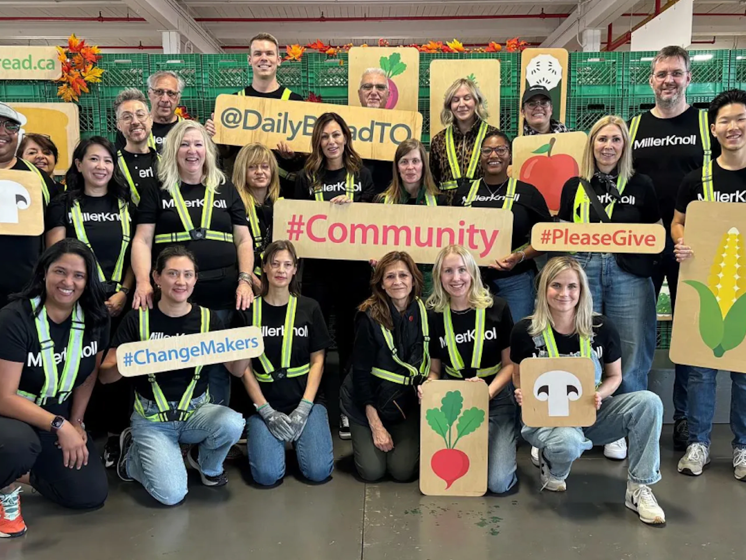 A group of MillerKnoll associates who volunteered at the Daily Bread Food Bank holding wood signs that show images of food.