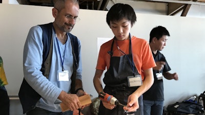 Two people at the Kidsdoor Tokyo design camp hosted by MillerKnoll. One holds a power drill while the other holds a block of wood.